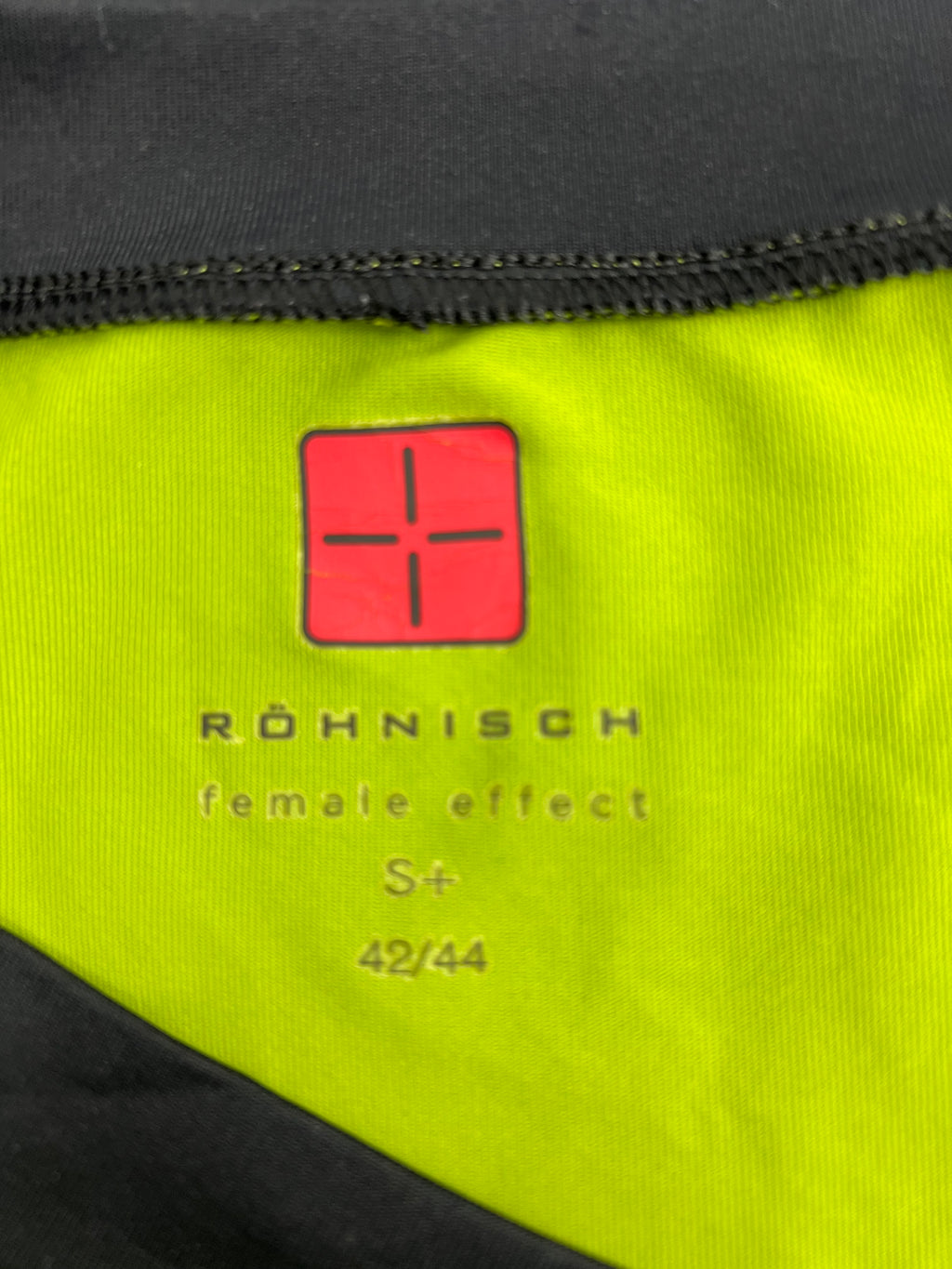 Close-up of Röhnisch brand logo and size label inside the green V-neck t-shirt