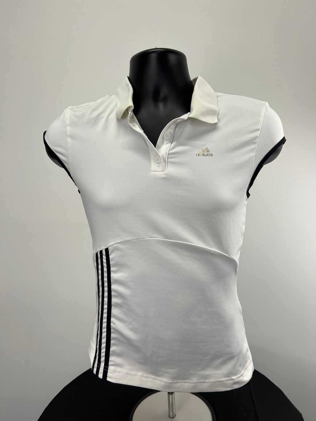 Front view of adidas women’s white tennis polo top with black trimmed sleeves and three black stripes on the side