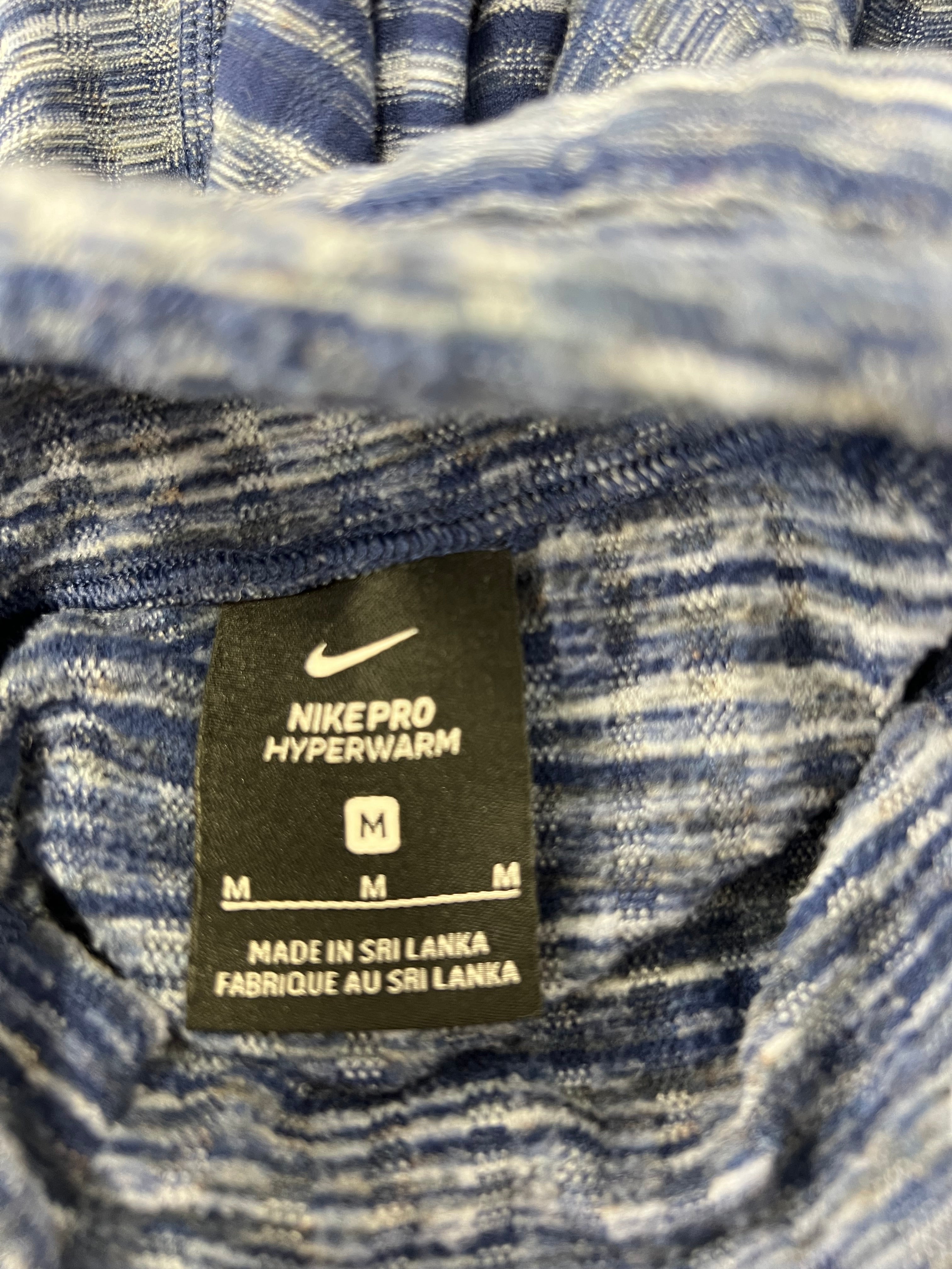 Close-up image of Nike Pro HyperWarm label inside the blue funnel neck top size medium