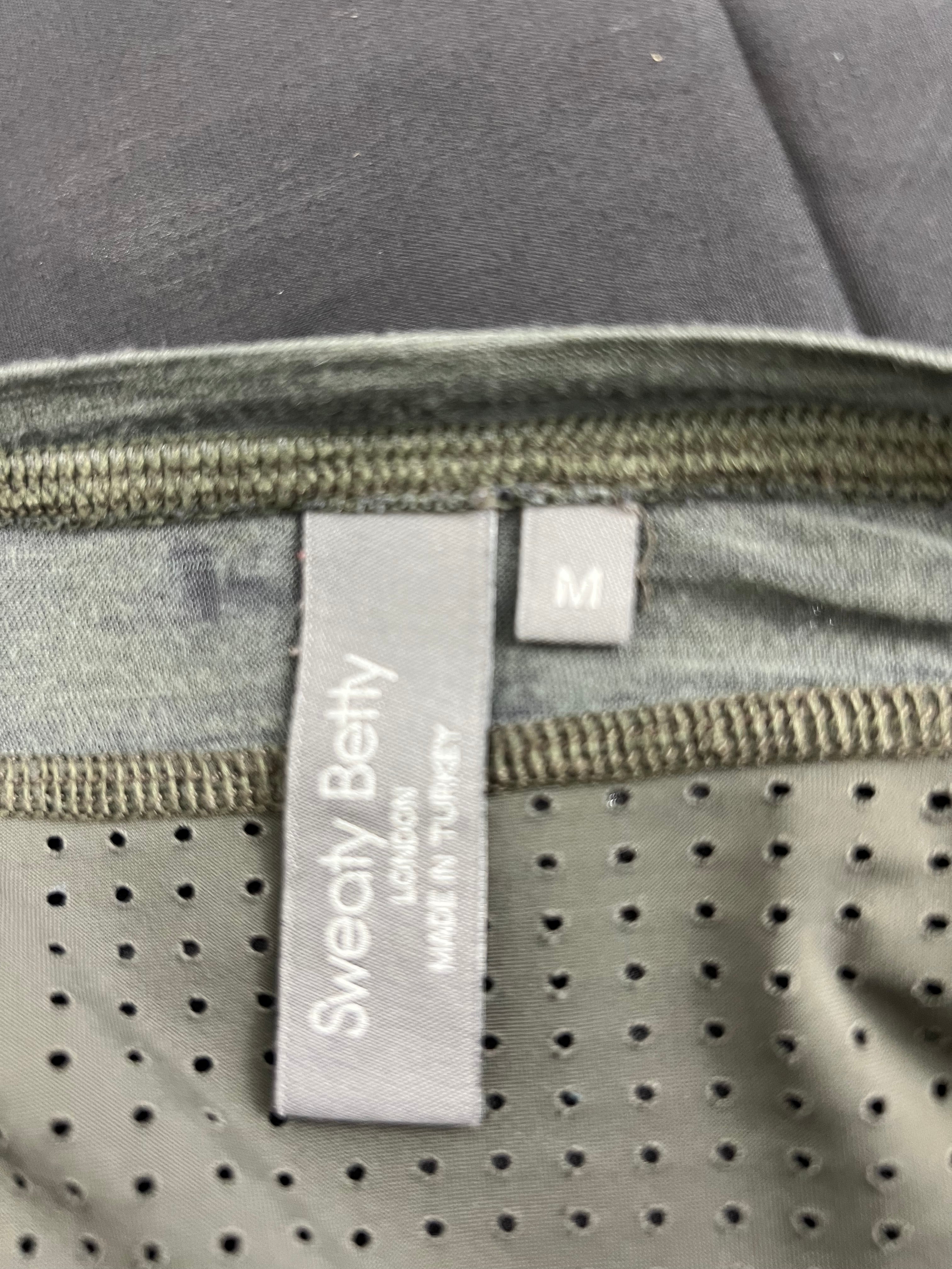 Close-up of Sweaty Betty brand label with size M on the inside collar of grey perforated long sleeve top
