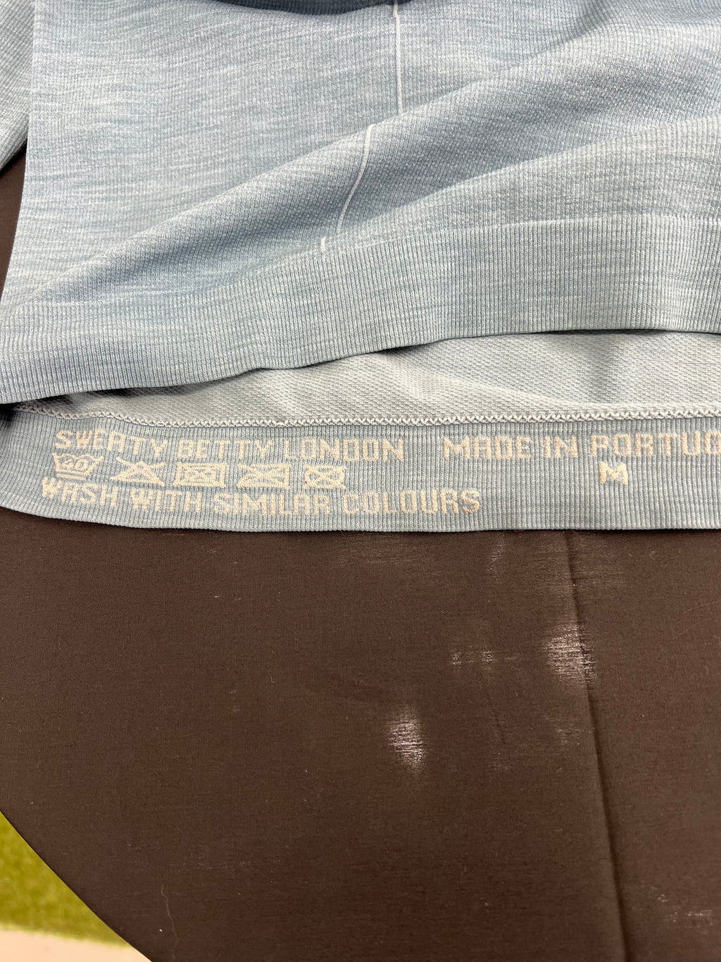 Close-up image of care label inside light blue Sweaty Betty long sleeve top showing washing instructions and size M