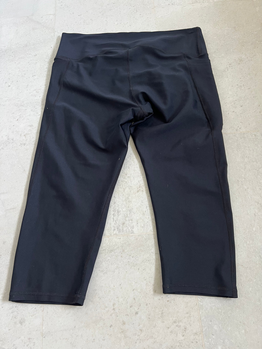 Under Armour black cropped compression leggings laid flat showing back side