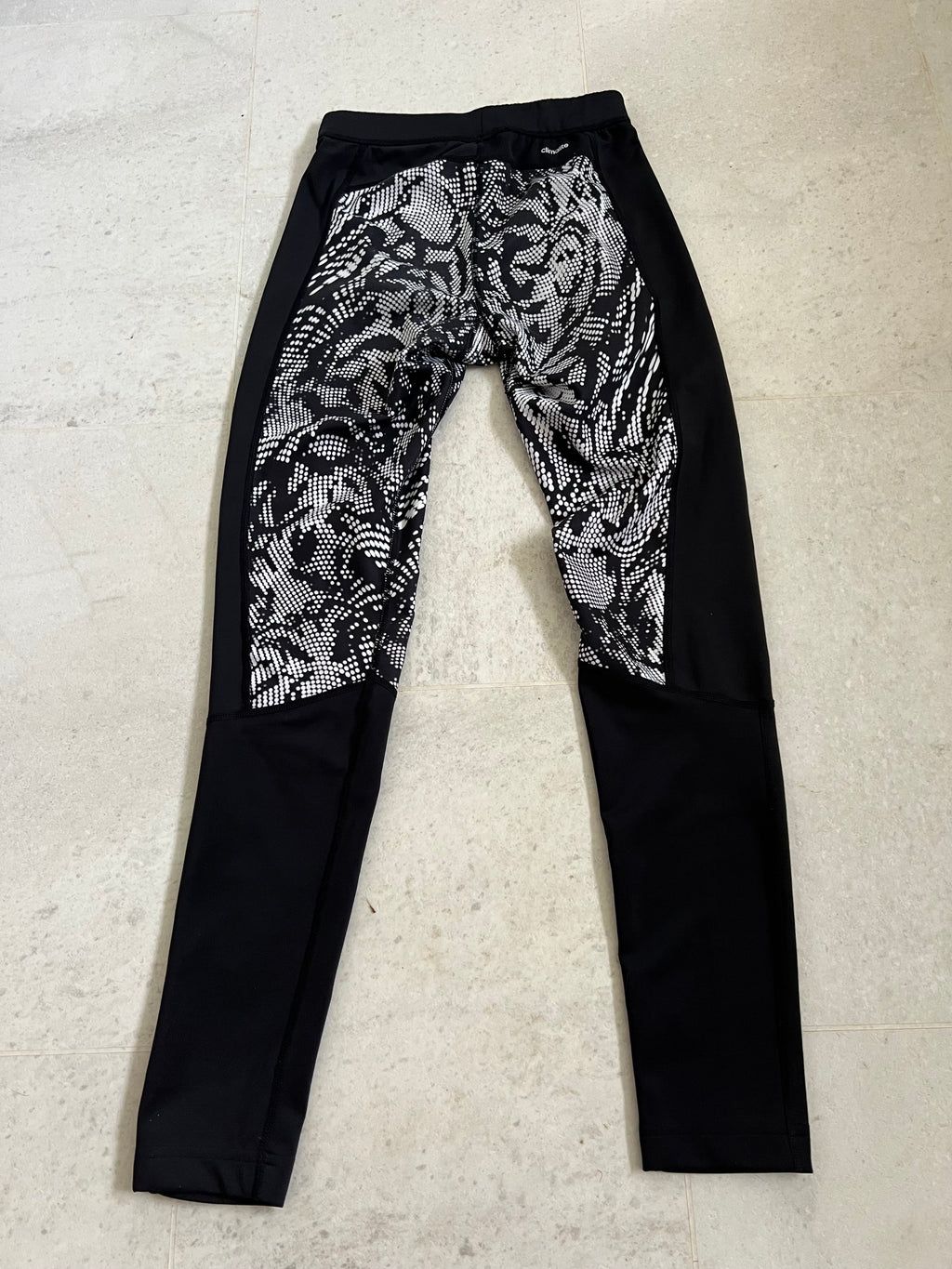 rear view of adidas Techfit leggings showing black and white patterned panels with black side panels on a tiled surface