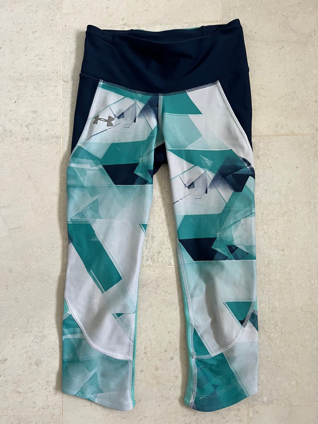Front view of Under Armour cropped compression leggings in size XS with teal and navy geometric print