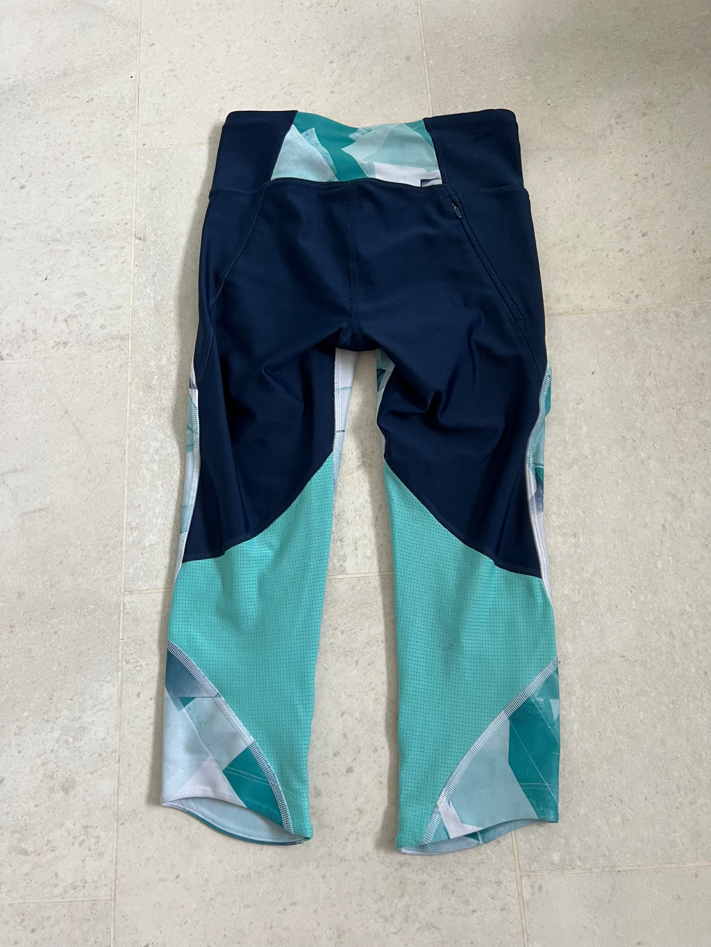 Back view of Under Armour cropped compression leggings showing solid navy fabric and teal mesh ventilation panels