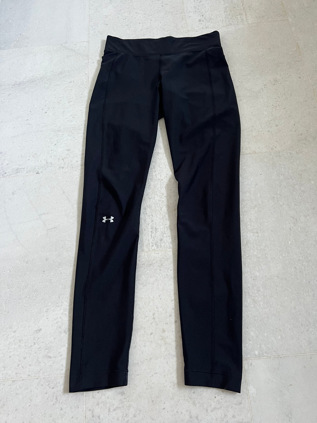 Front view of Under Armour black compression leggings laid flat
