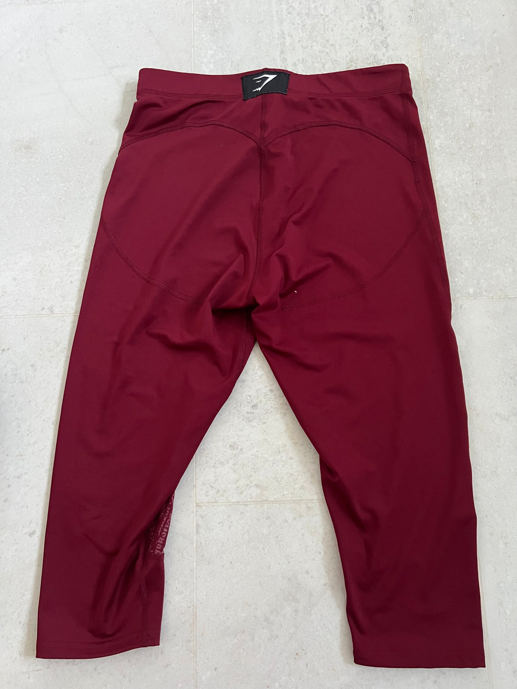 Back view of burgundy Gymshark cropped leggings showing logo patch on waistband