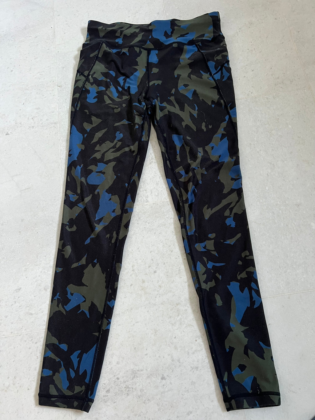 Front view of Sweaty Betty full length leggings in camouflage print with shades of black, green, and blue laid flat