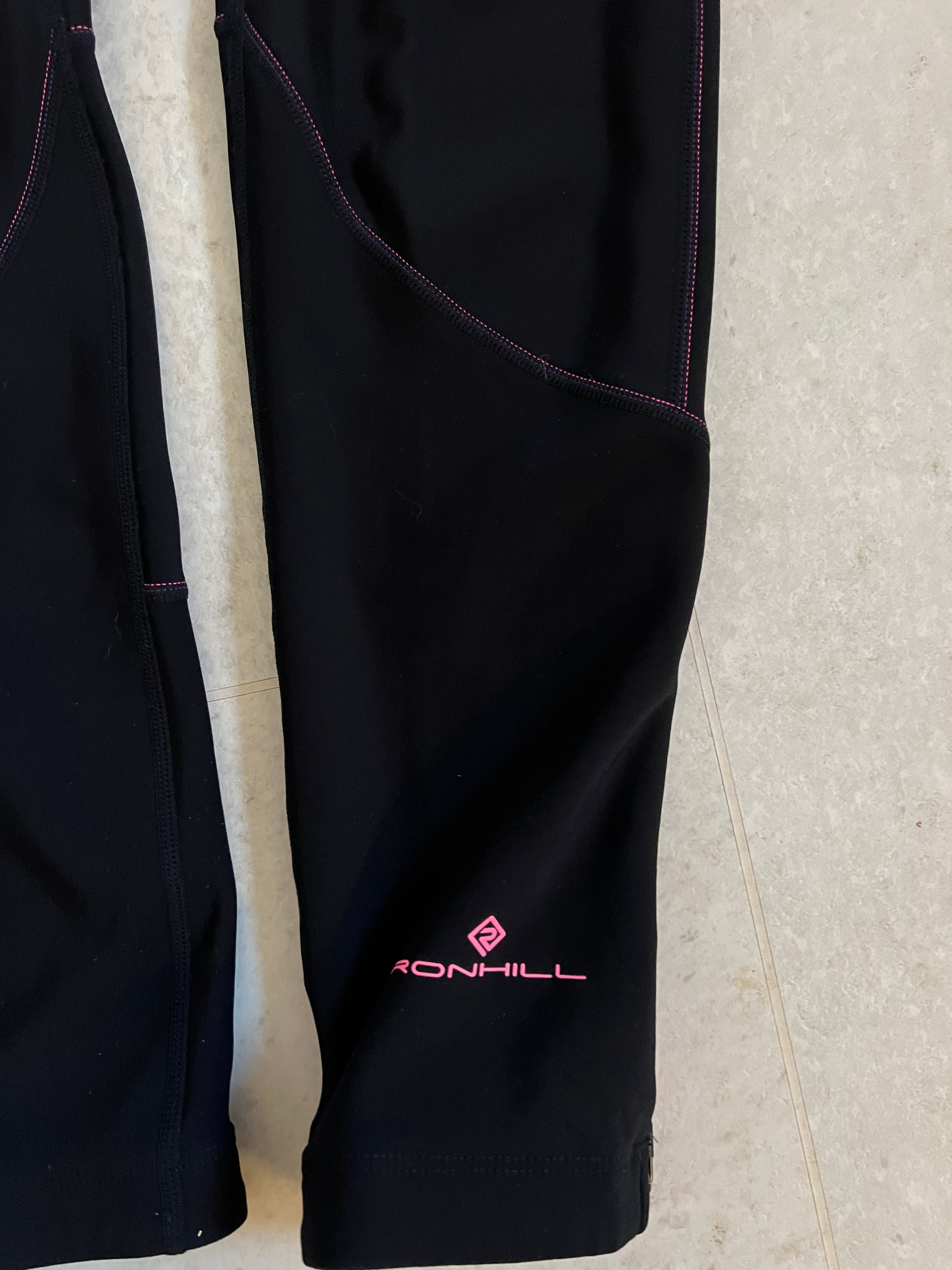 Close-up of Ronhill logo and leg detail on black running tights with pink stitching and reflective print