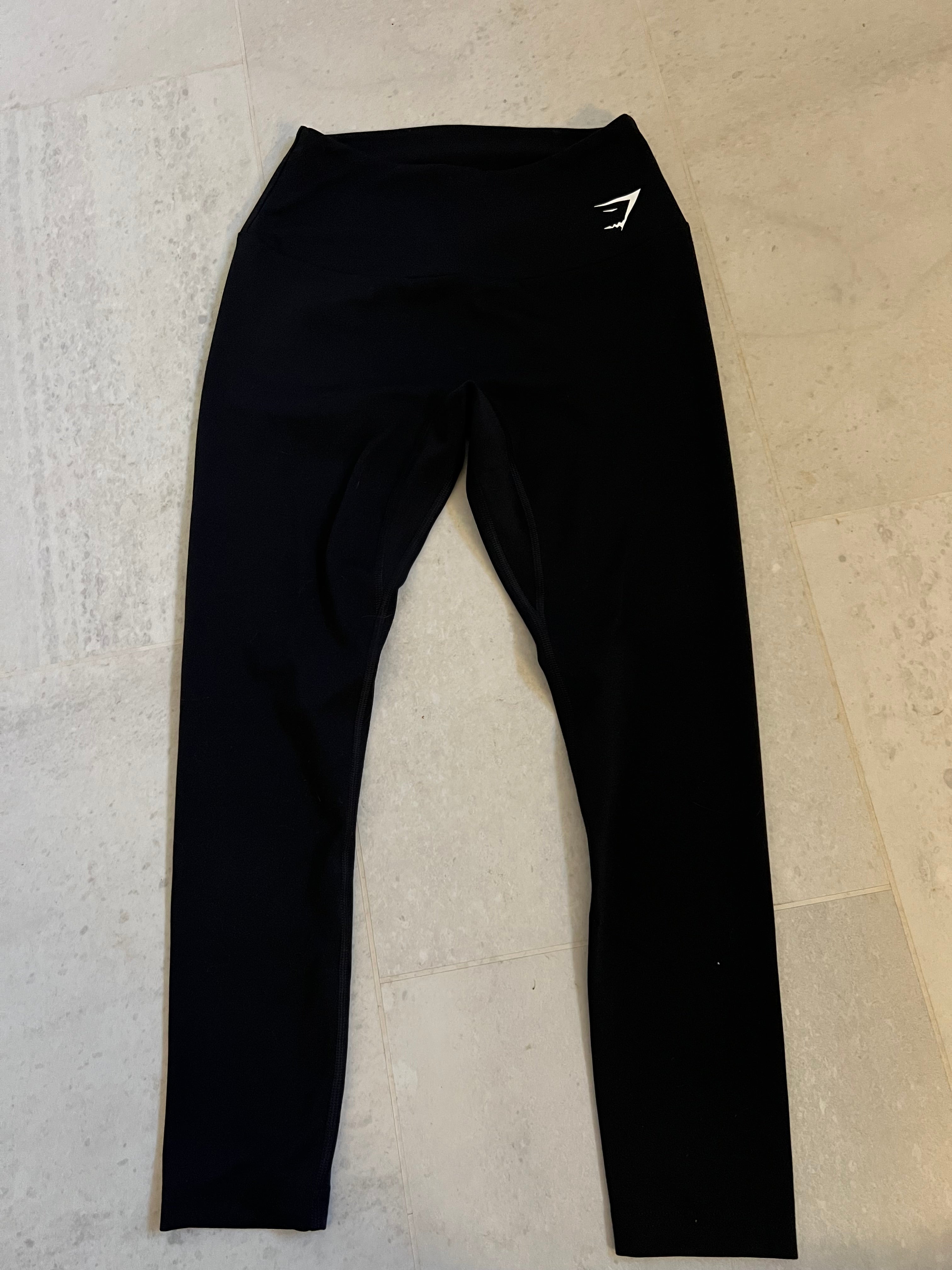 Front view of black Gymshark cropped leggings laid flat on light flooring