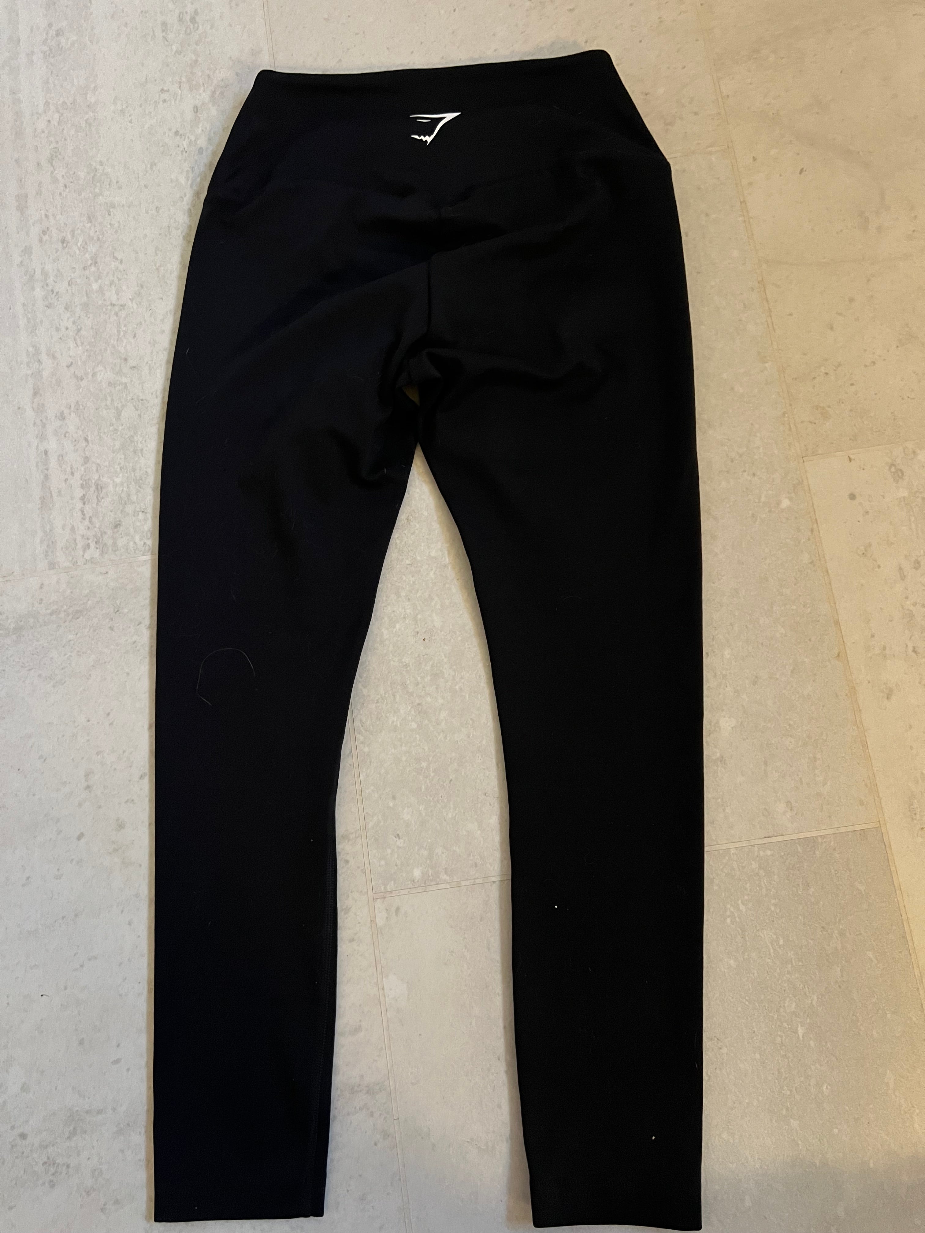 Back view of black Gymshark cropped leggings laid flat on light flooring