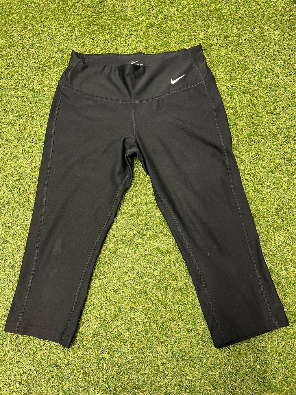 Front view of Nike Dri-FIT black cropped leggings laid flat on grass