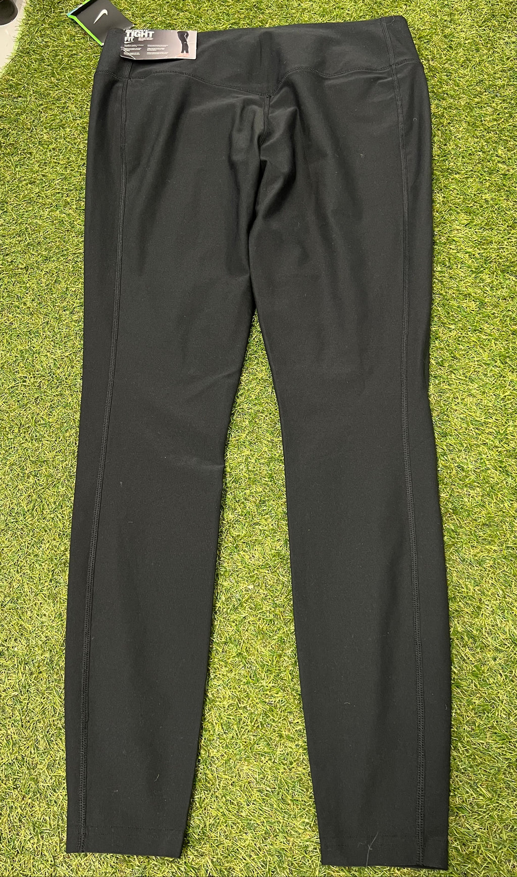 Nike black Dri-FIT leggings laid flat on green surface back view showing stitching