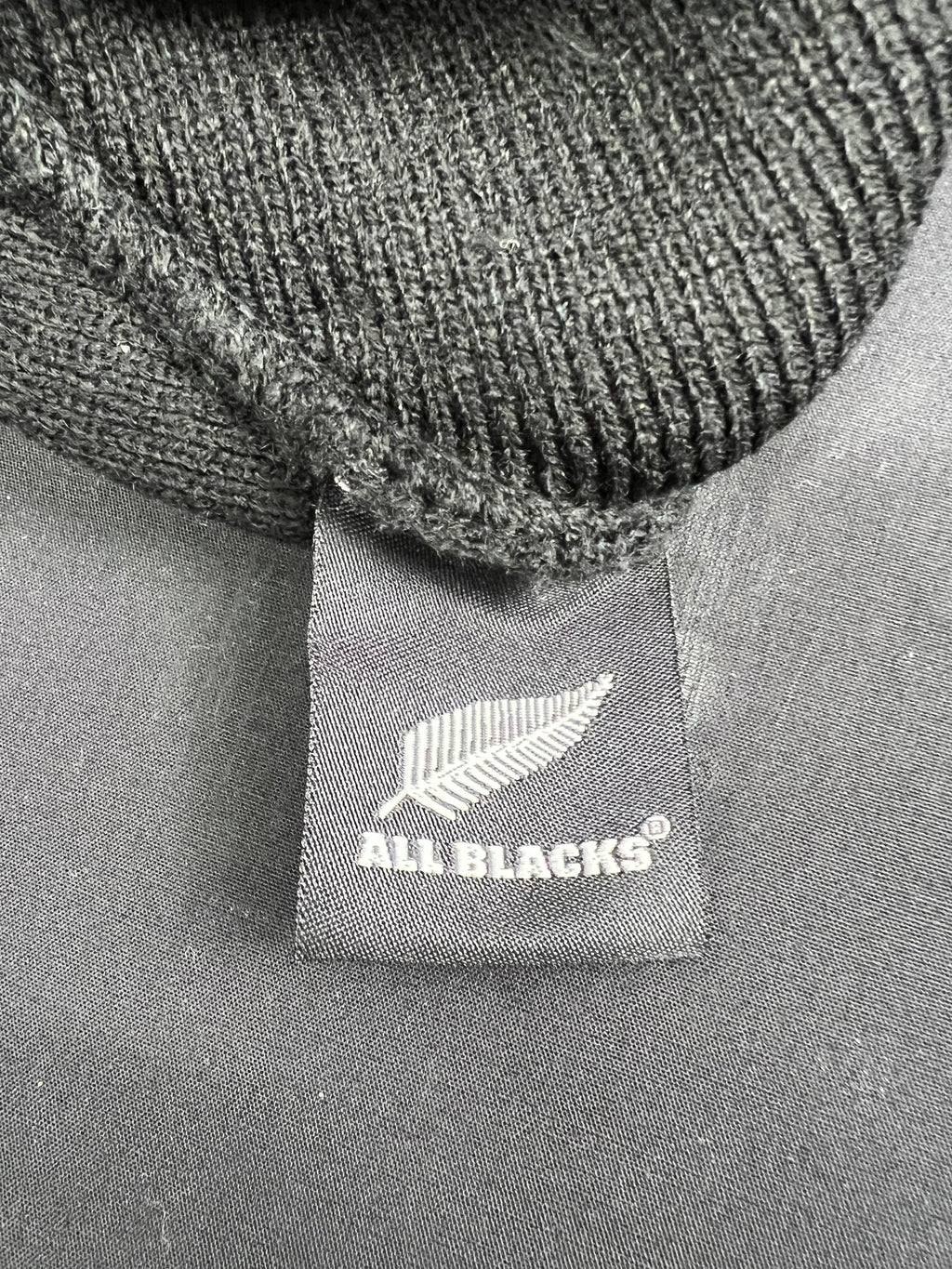 Close-up of All Blacks tag sewn inside black knit beanie highlighting official branding