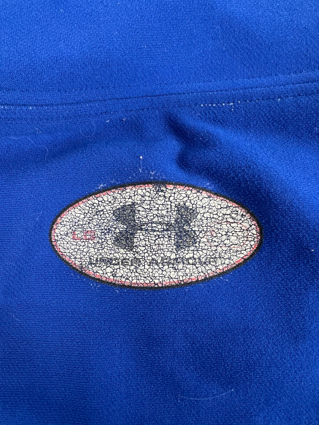 Close-up of faded Under Armour logo stamp on the back collar of the blue base layer top
