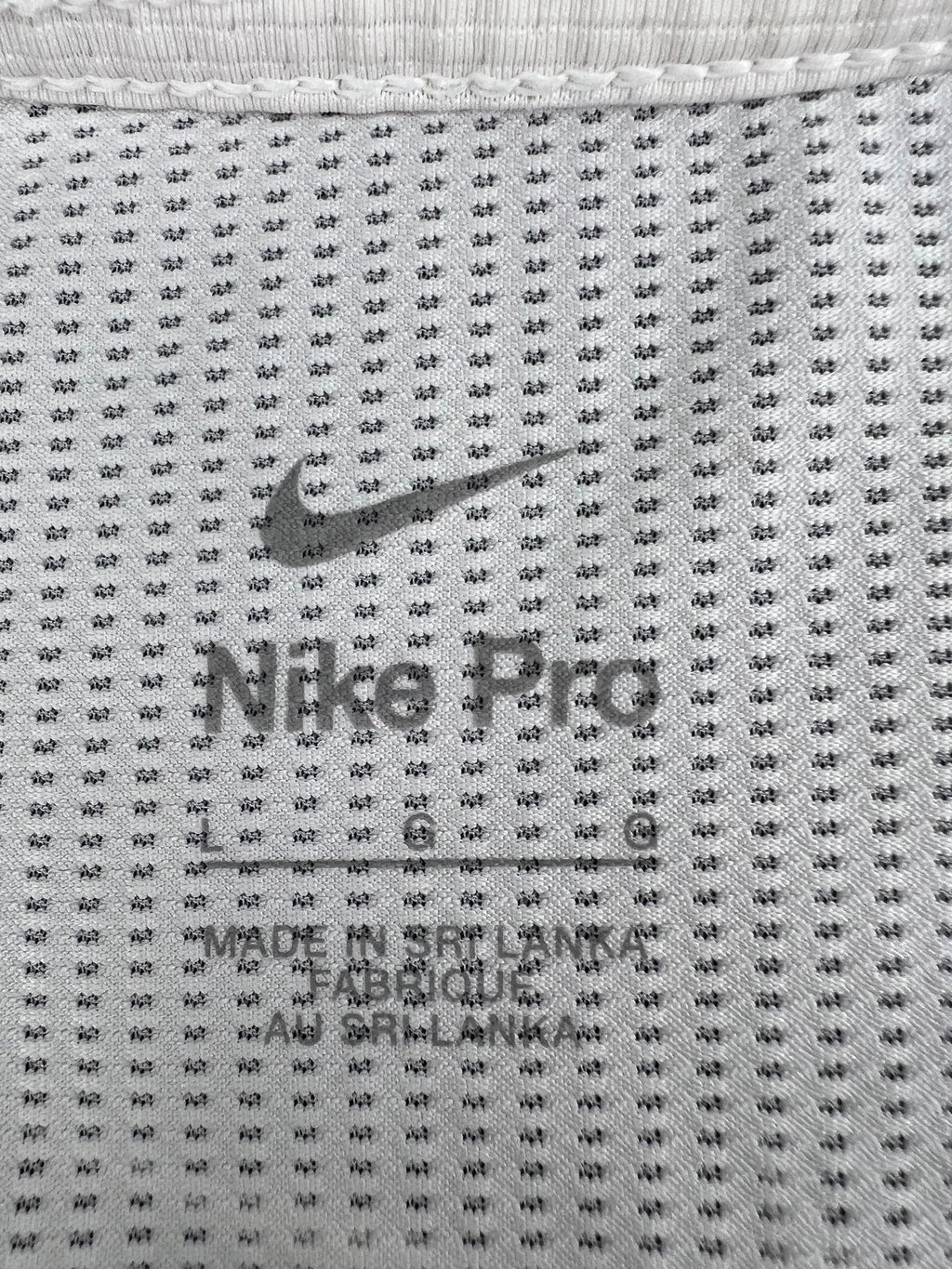 Close-up of Nike Pro size label printed on the inside mesh fabric of cream long sleeve top