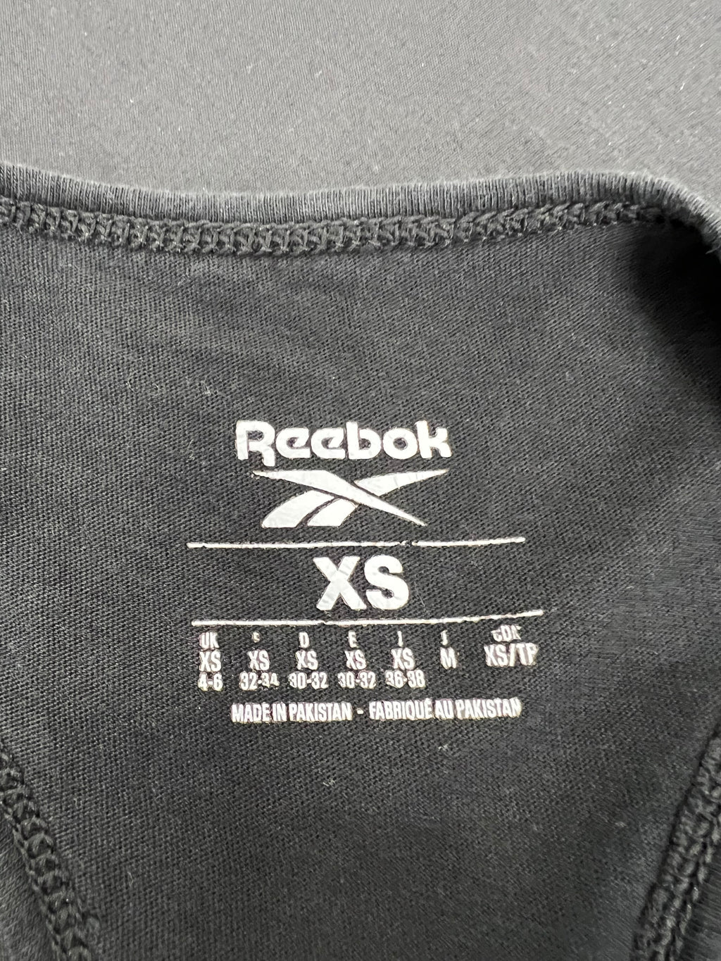 Close-up of size label inside black Reebok vest top showing XS size and manufacturing details