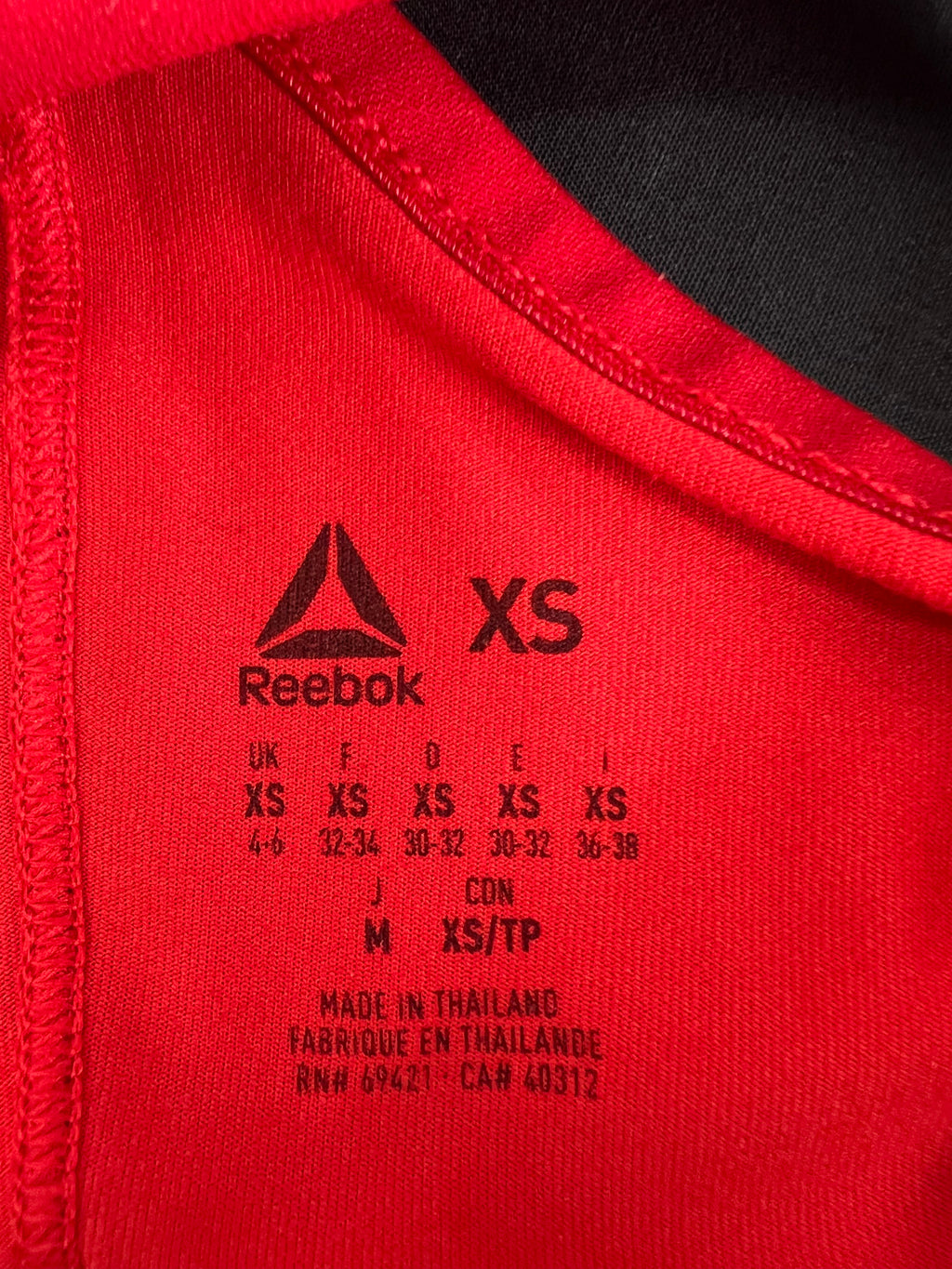 Close-up of size label inside red Reebok vest showing XS and care details