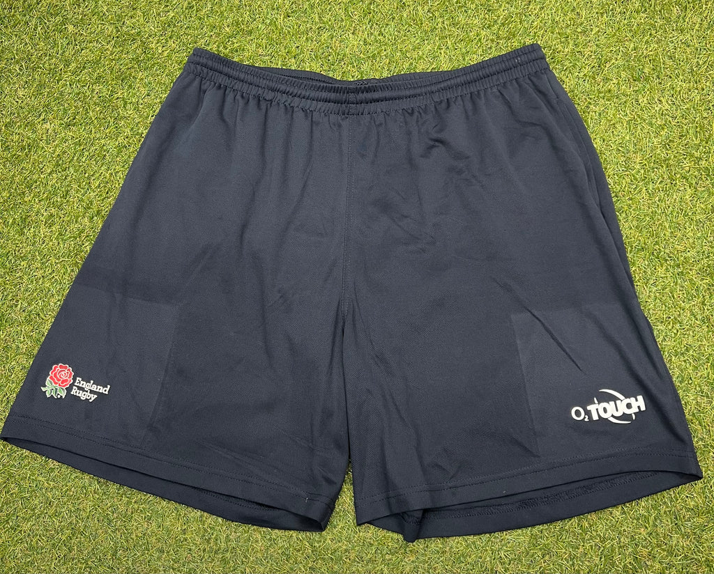 Front view of black England Rugby shorts with England rose logo and O2 Touch branding on a grass background
