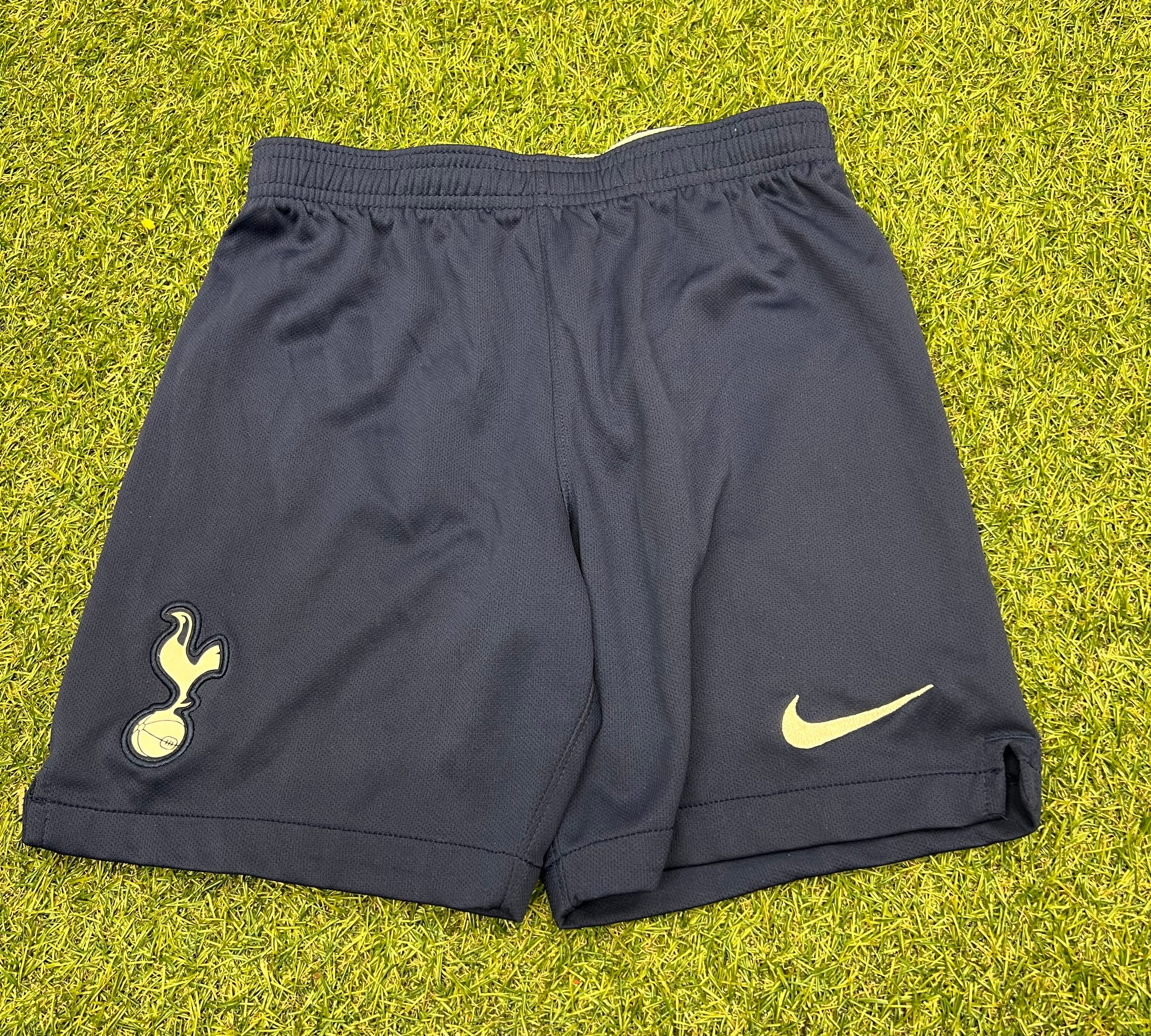 Front view of kids Tottenham Hotspur navy blue football shorts on grass