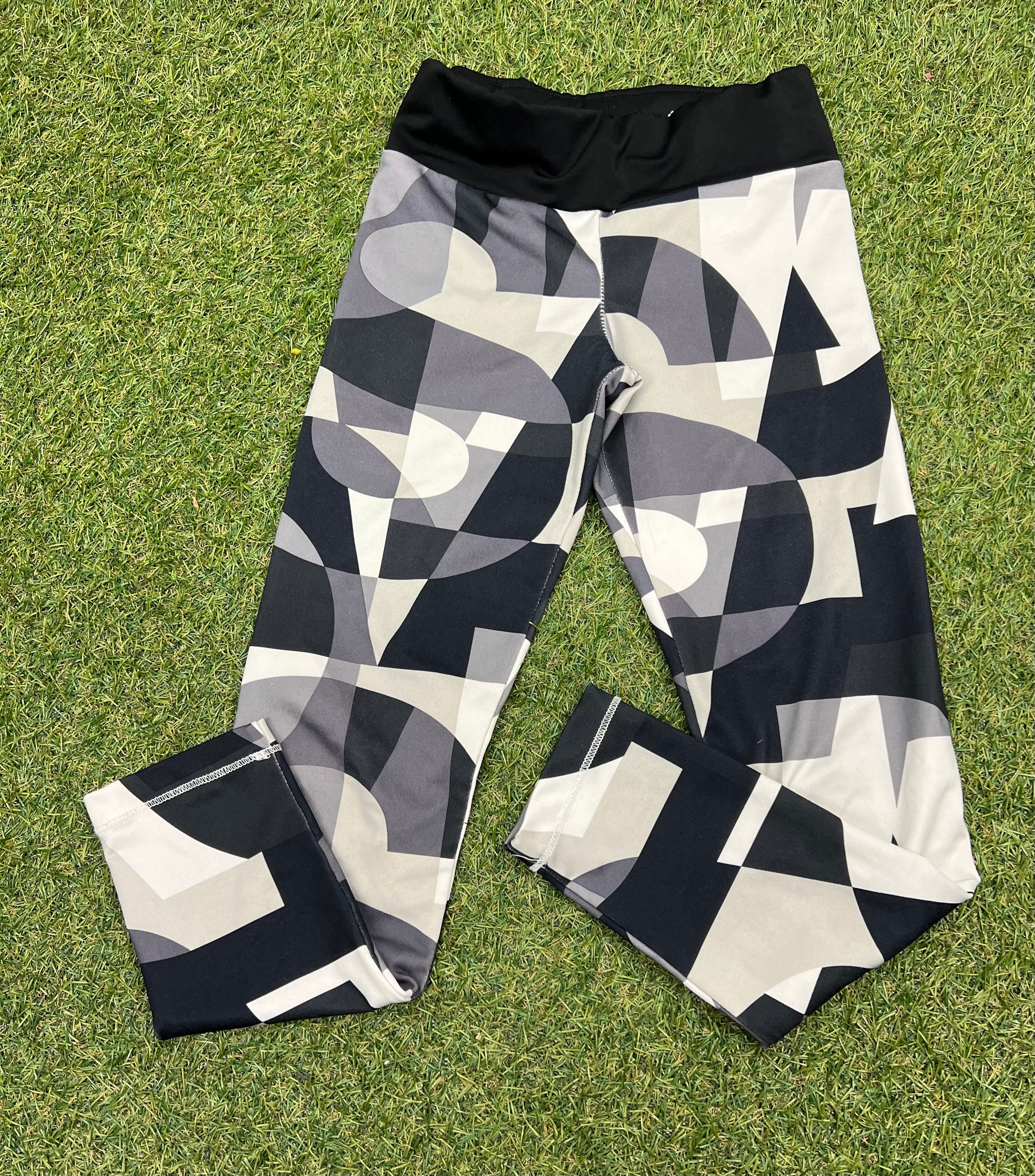 Front view of adidas kids leggings with geometric black, grey, and white pattern on grass
