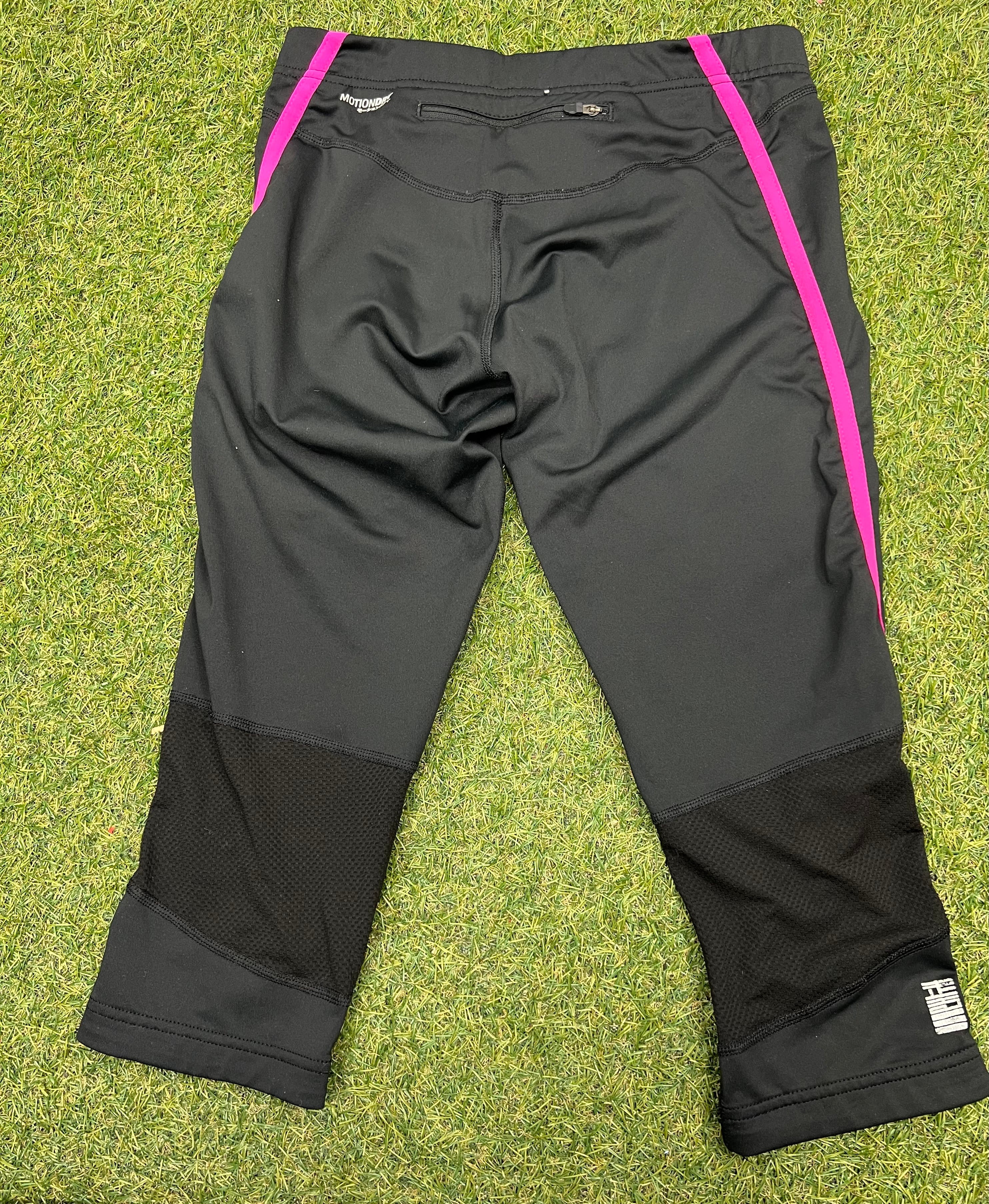 Back view of Asics black cropped leggings showing zip pocket and mesh panels on grass