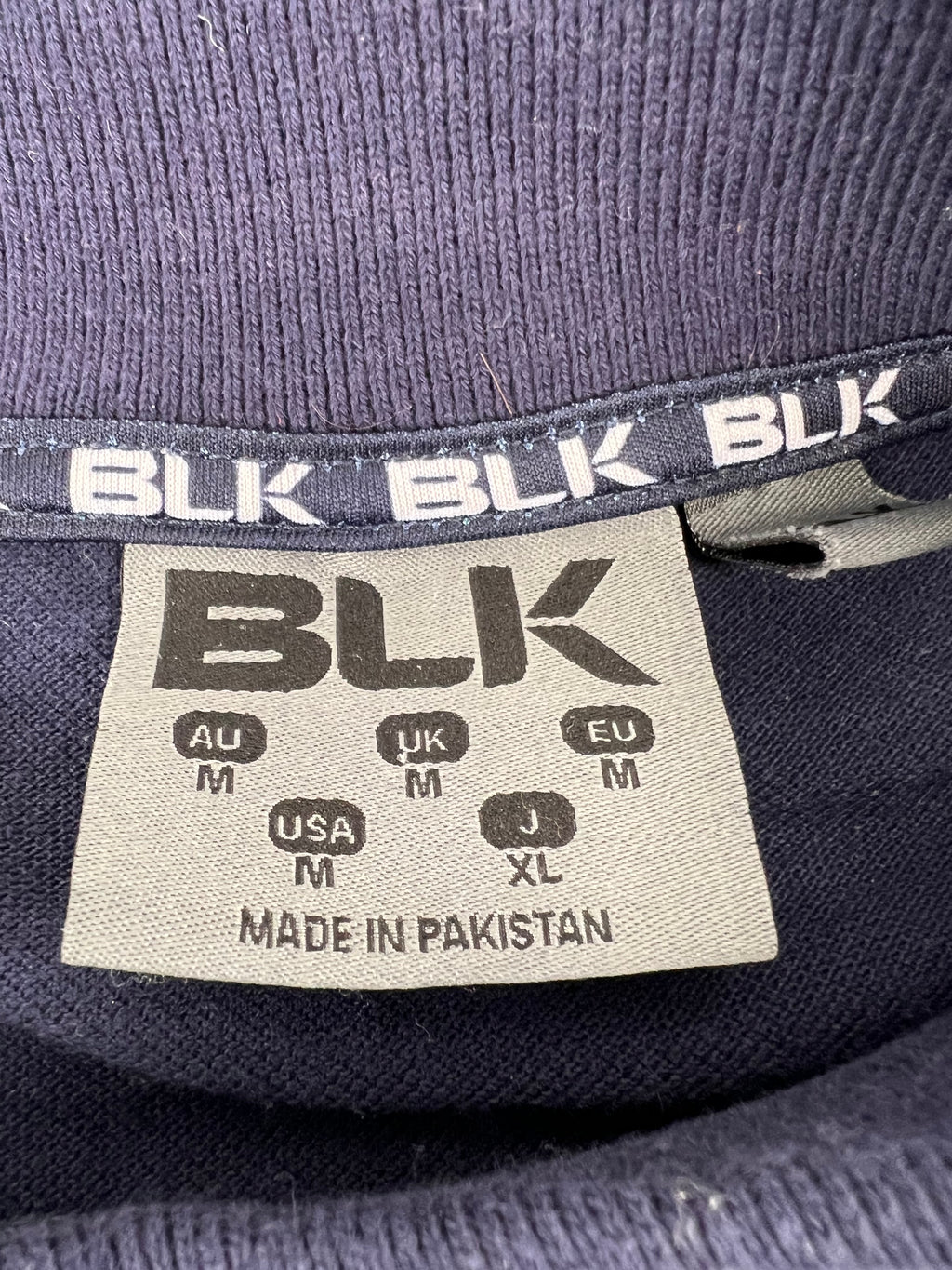 Close-up of BLK size tag inside navy rugby polo indicating medium size and made in Pakistan