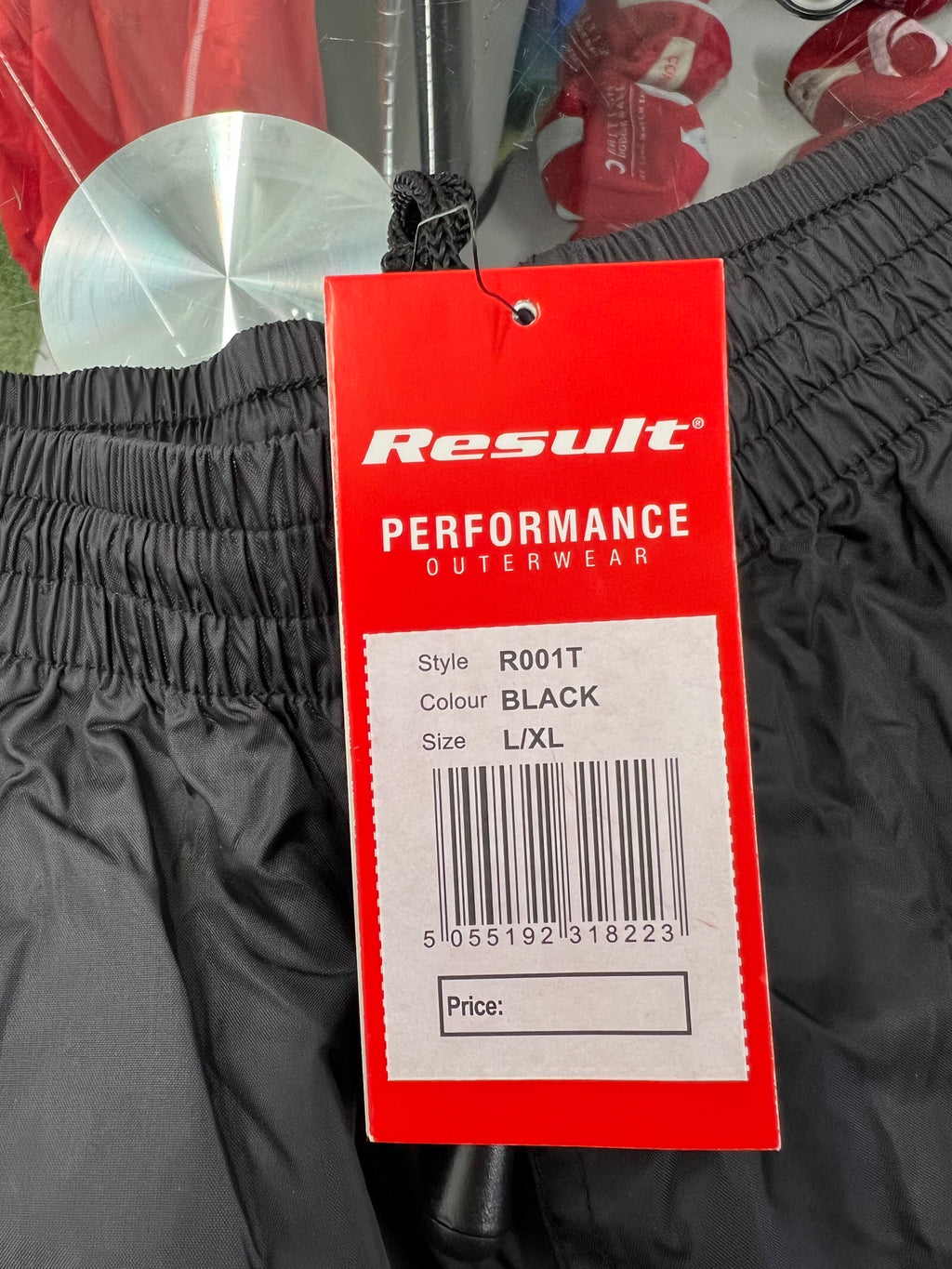 Close-up of red Result Performance outerwear tag showing size L/XL and black colour on London Irish waterproof trousers