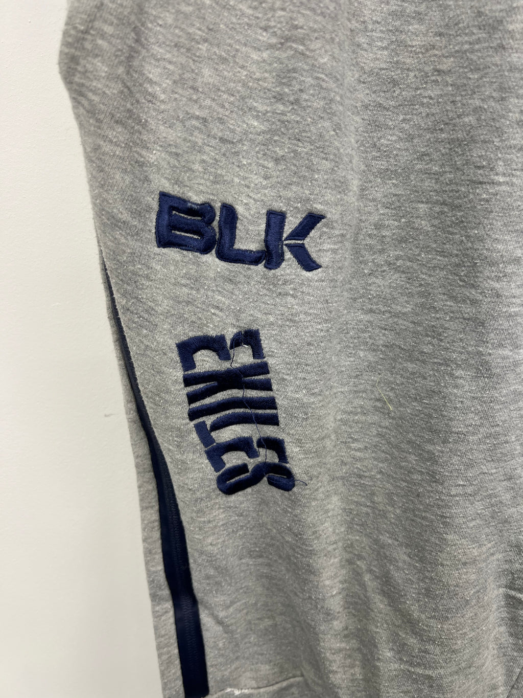 Close-up side view of BLK and Exiles navy blue embroidery on grey tracksuit trousers