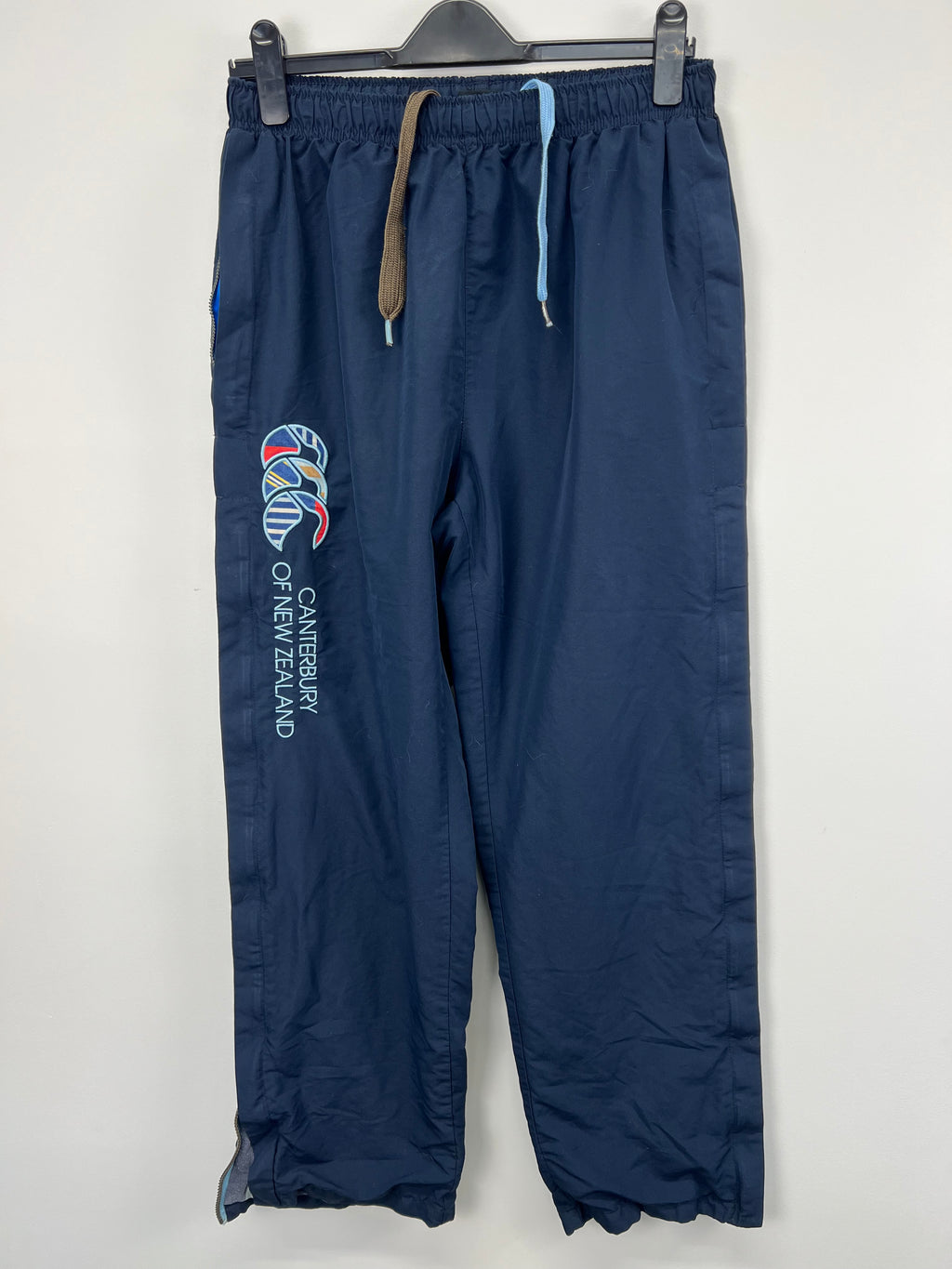 Front view of men's navy blue Canterbury of New Zealand tracksuit trousers hanging on hanger
