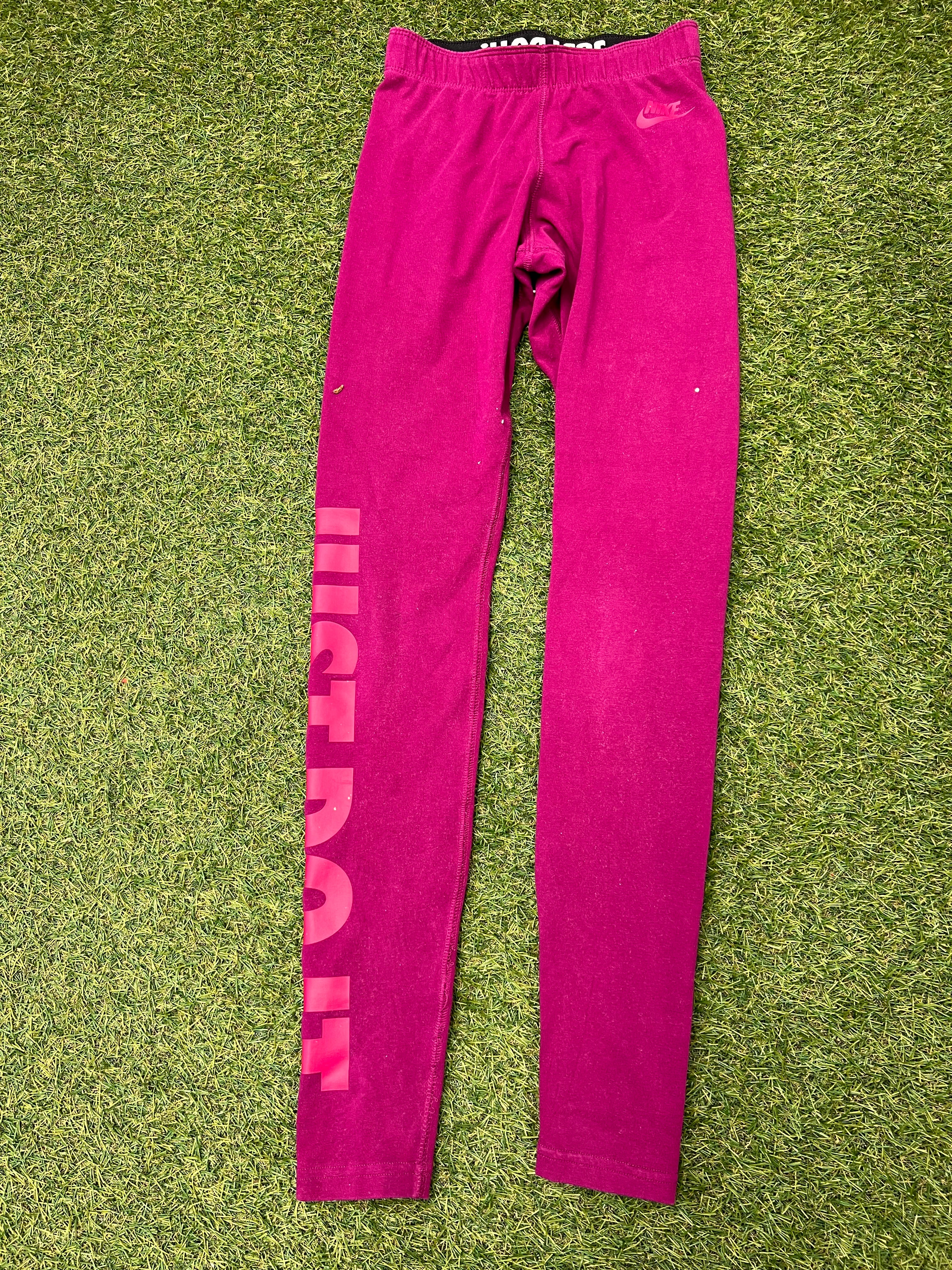 Nike bright pink leggings with Just Do It print down left leg laid flat on grass front view