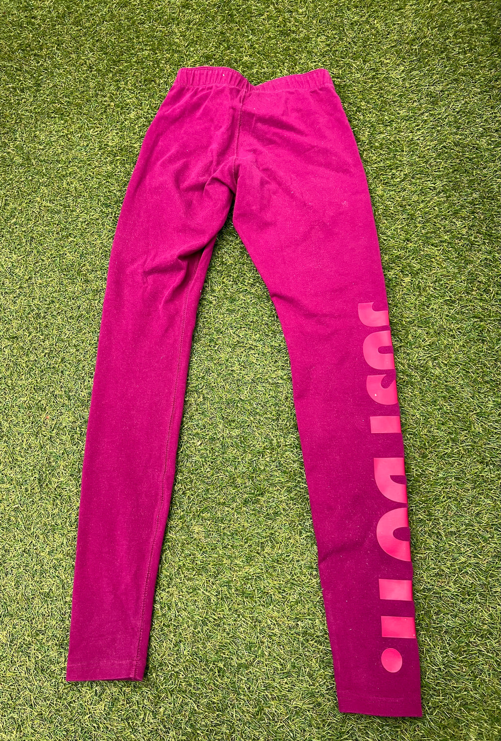 Nike bright pink leggings with Just Do It print down left leg laid flat on grass back view