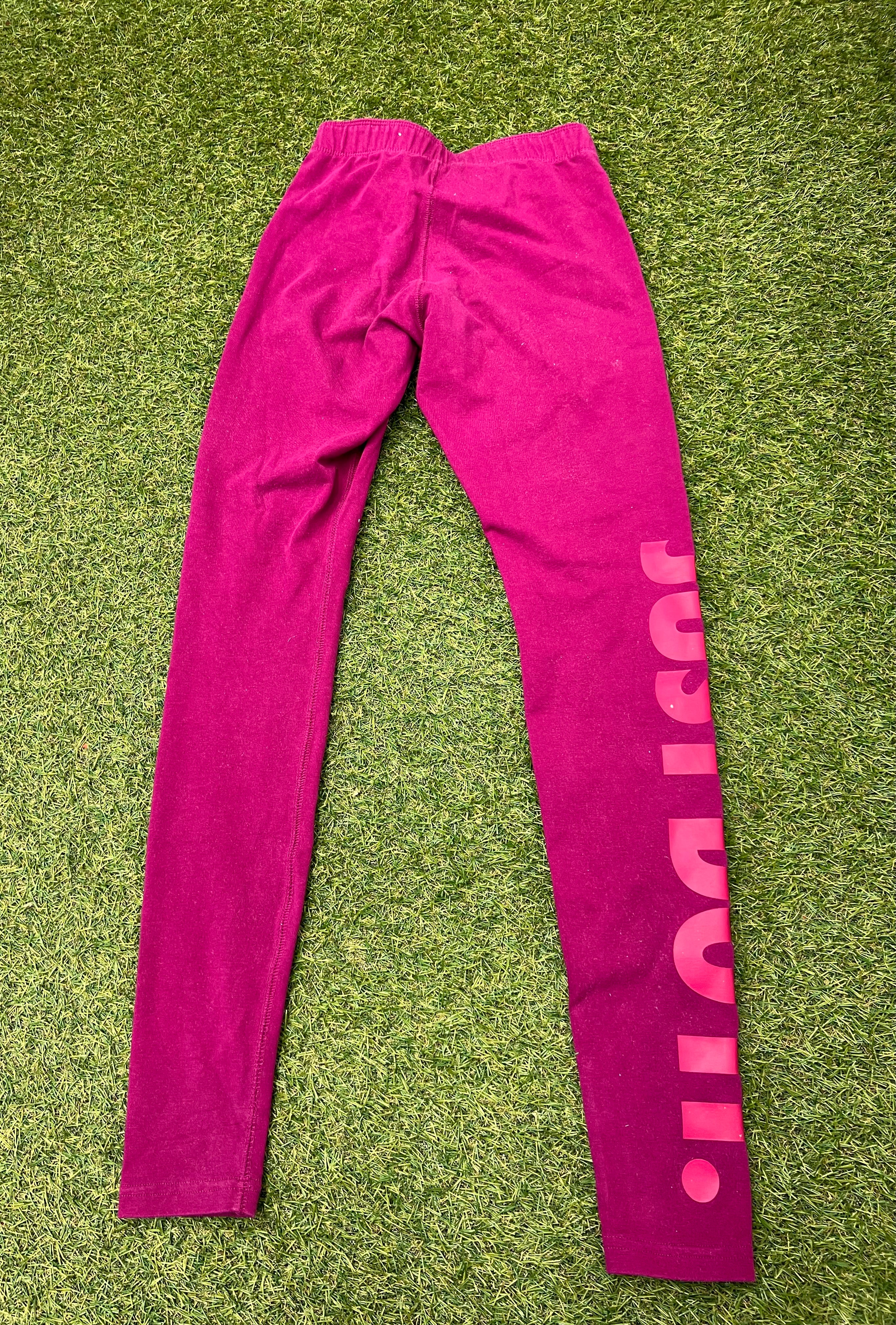 Nike bright pink leggings with Just Do It print down left leg laid flat on grass back view