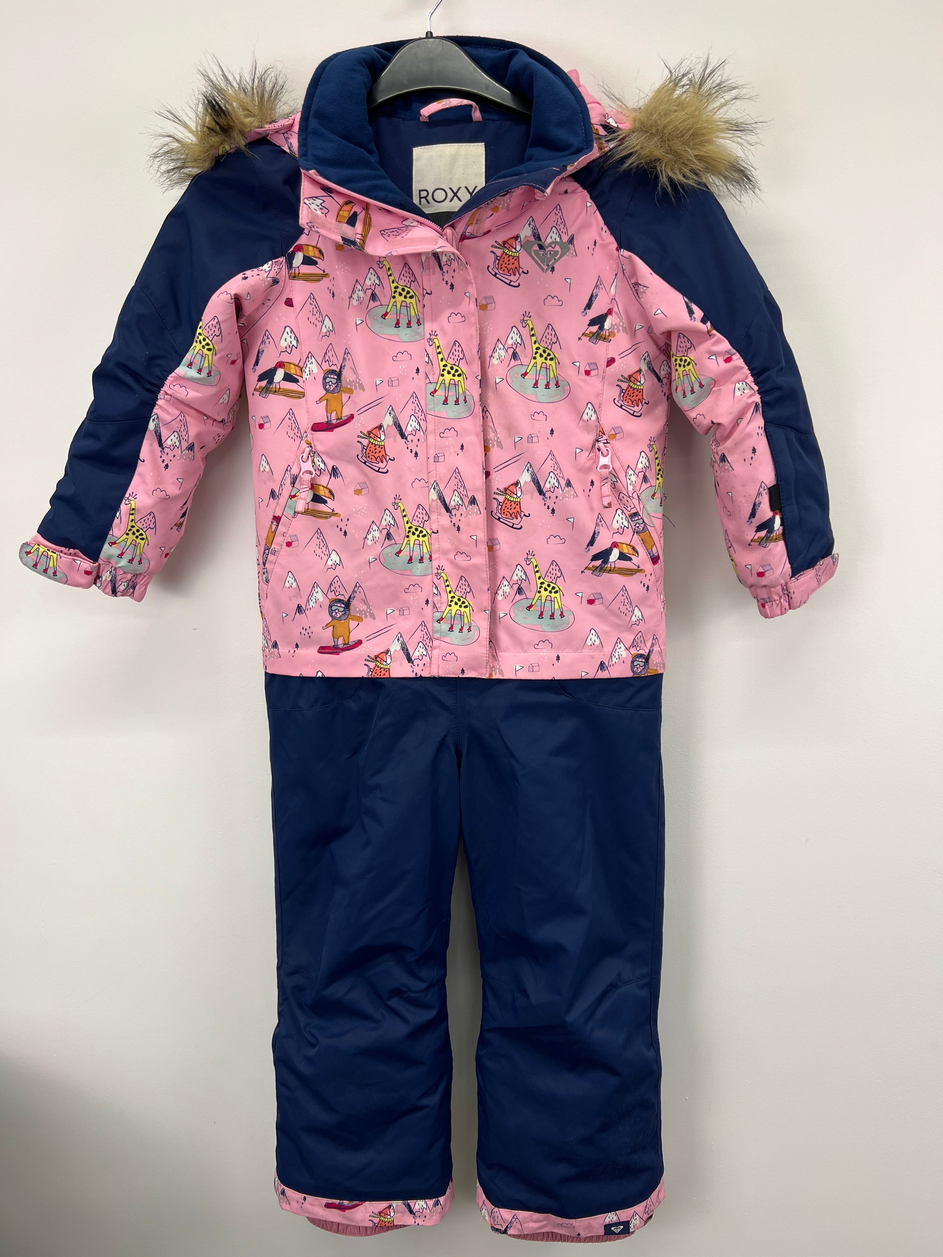 Front view of Roxy kids snow suit featuring pink patterned jacket with giraffe and mountain prints and navy blue snow trousers