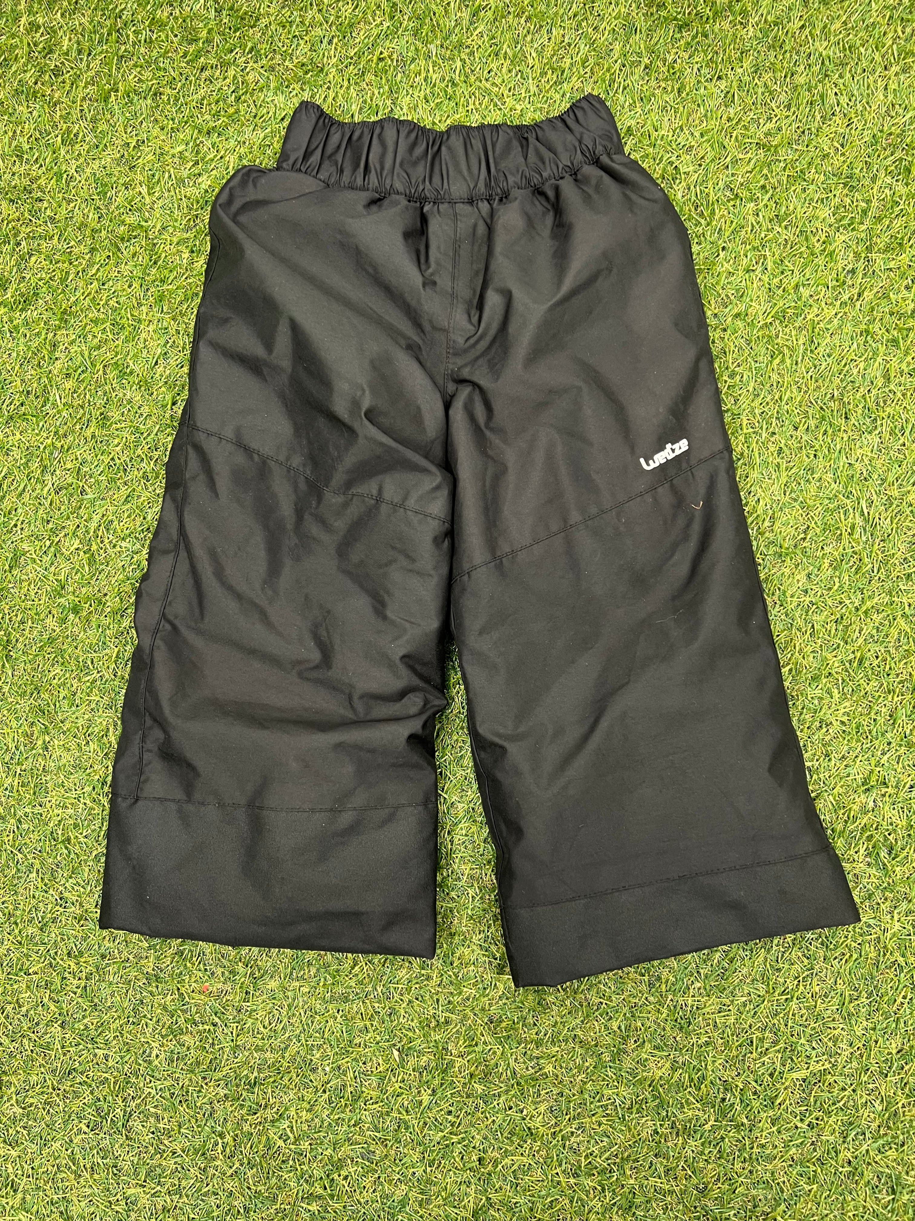 Front view of Decathlon kids black ski trousers laid flat on grass