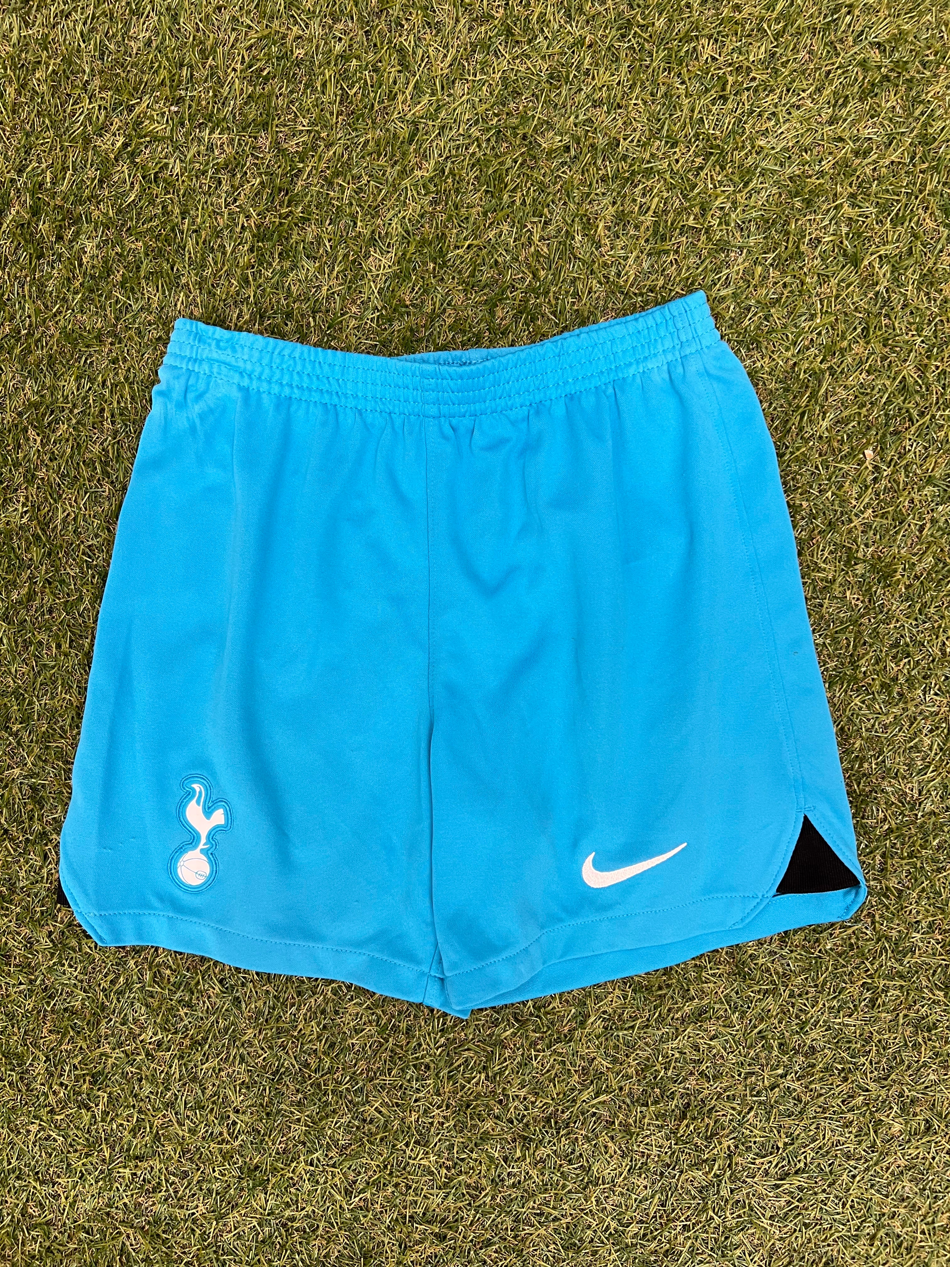 Front view of kids Tottenham Hotspur FC blue shorts laid on grass showing team crest and Nike logo