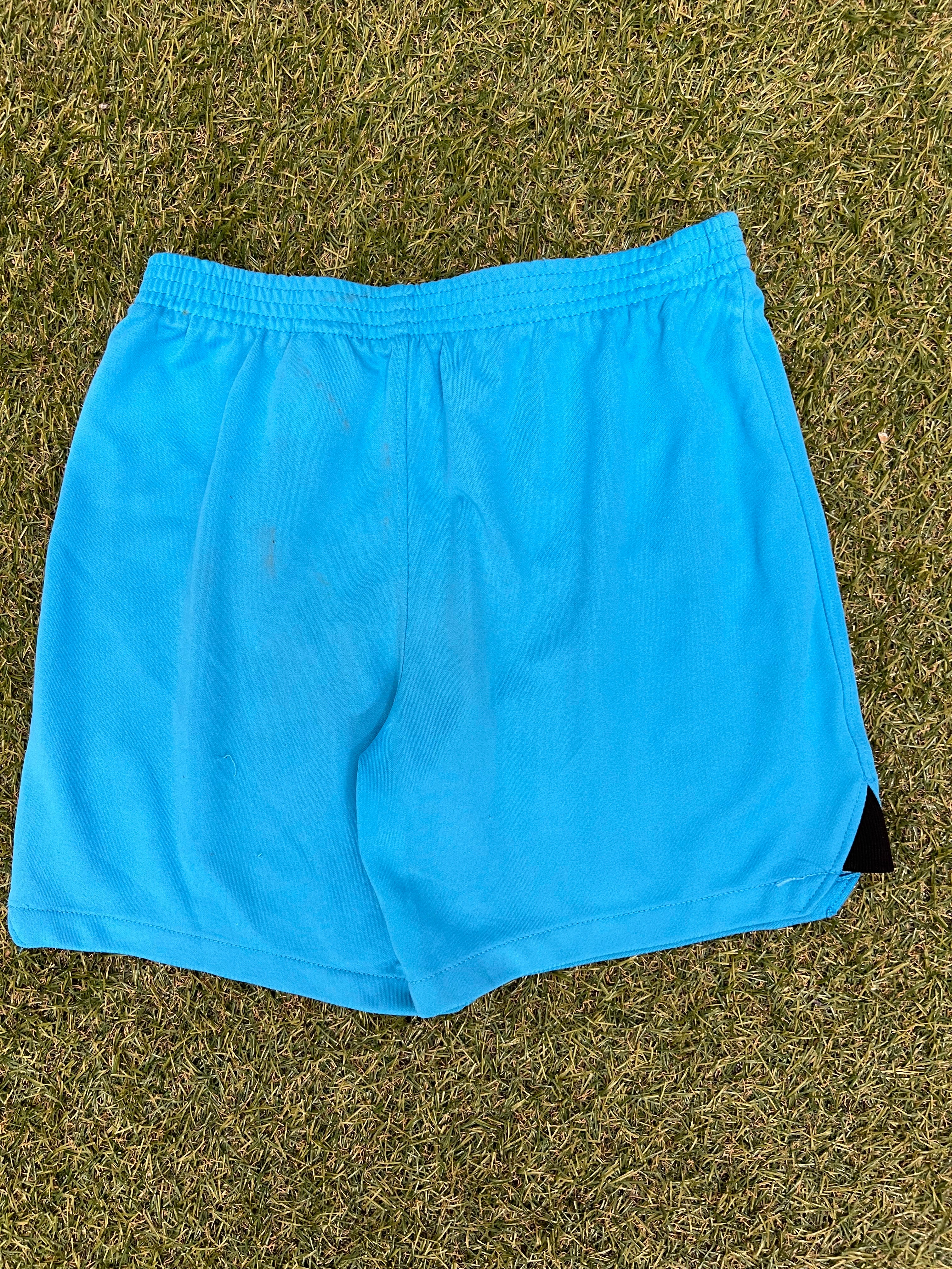 Back view of kids Tottenham Hotspur FC blue shorts laid on grass showing plain design