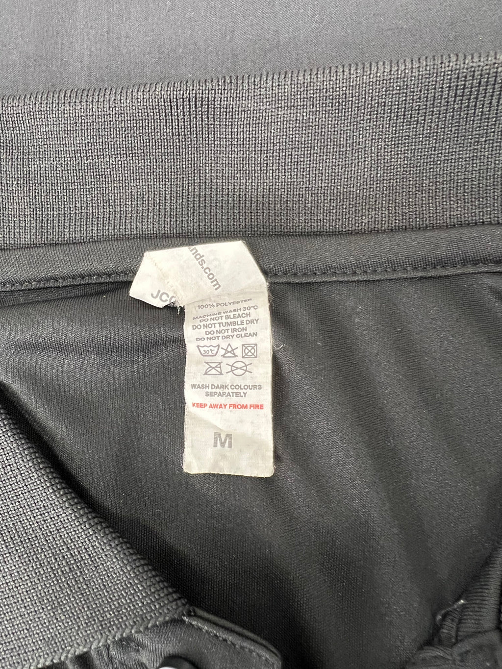 Care label showing 100% polyester material and washing instructions on Jamaica rugby polo shirt