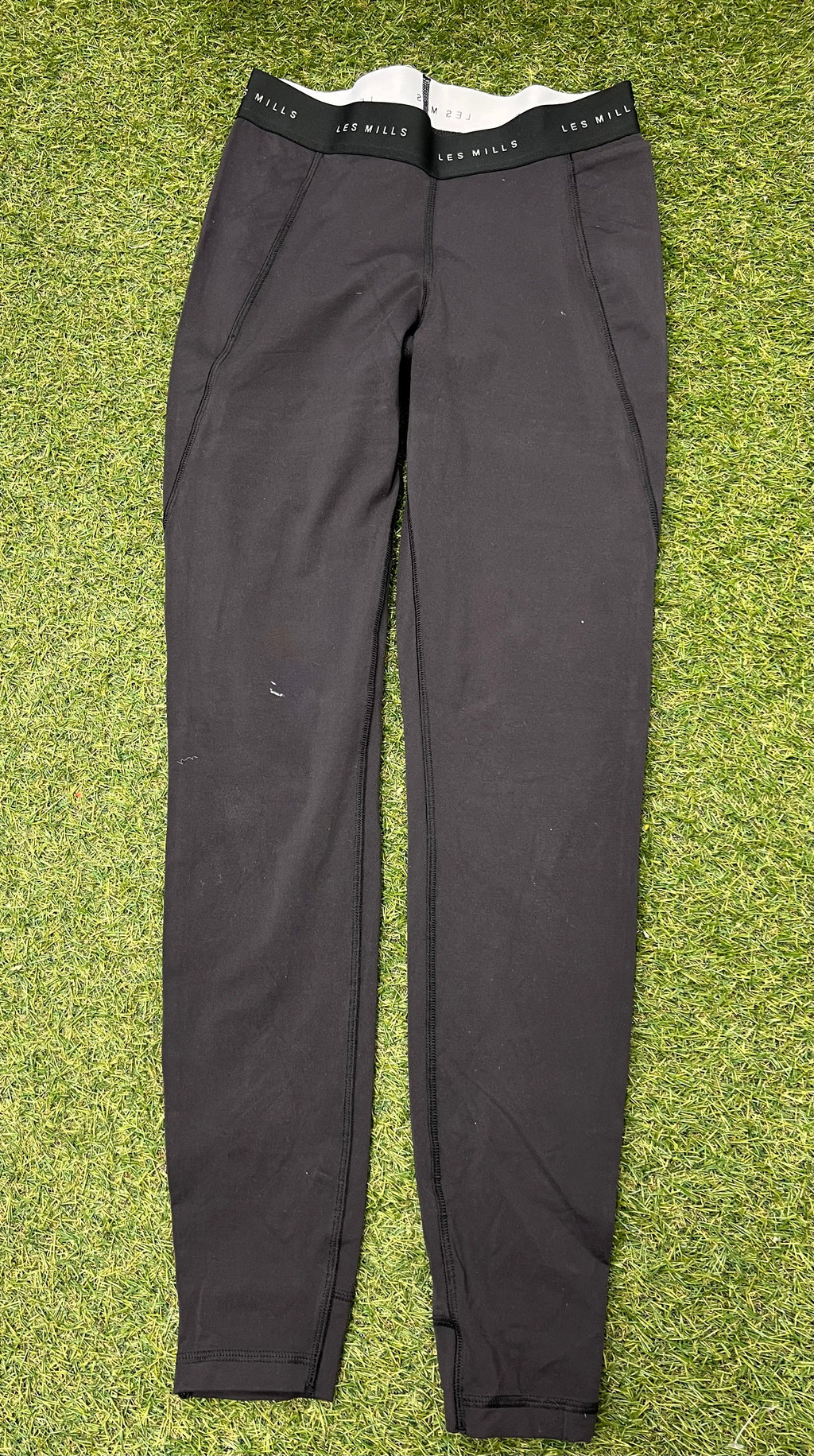 Front view of black Reebok x Les Mills Speedwick women's leggings laid flat on grass