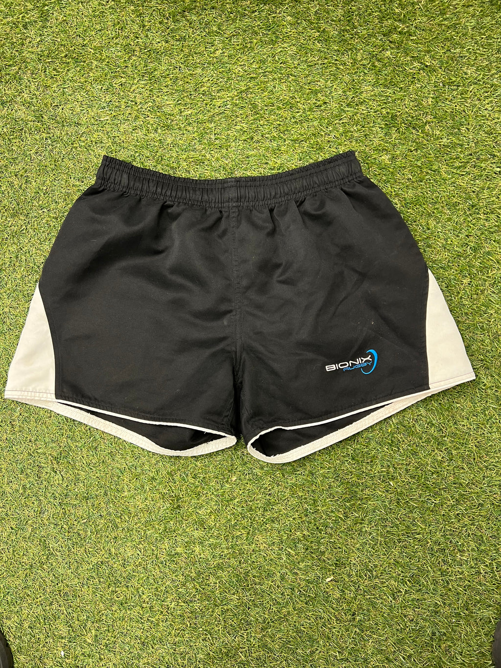 Front view of black Bionix rugby shorts with white side panels on grass