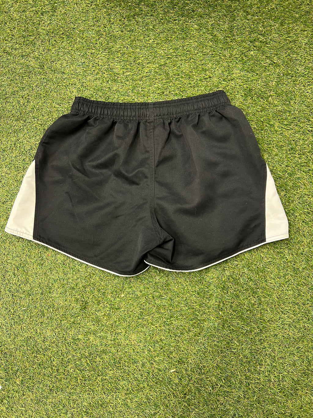 Back view of black rugby shorts with white side panels and elastic waistband