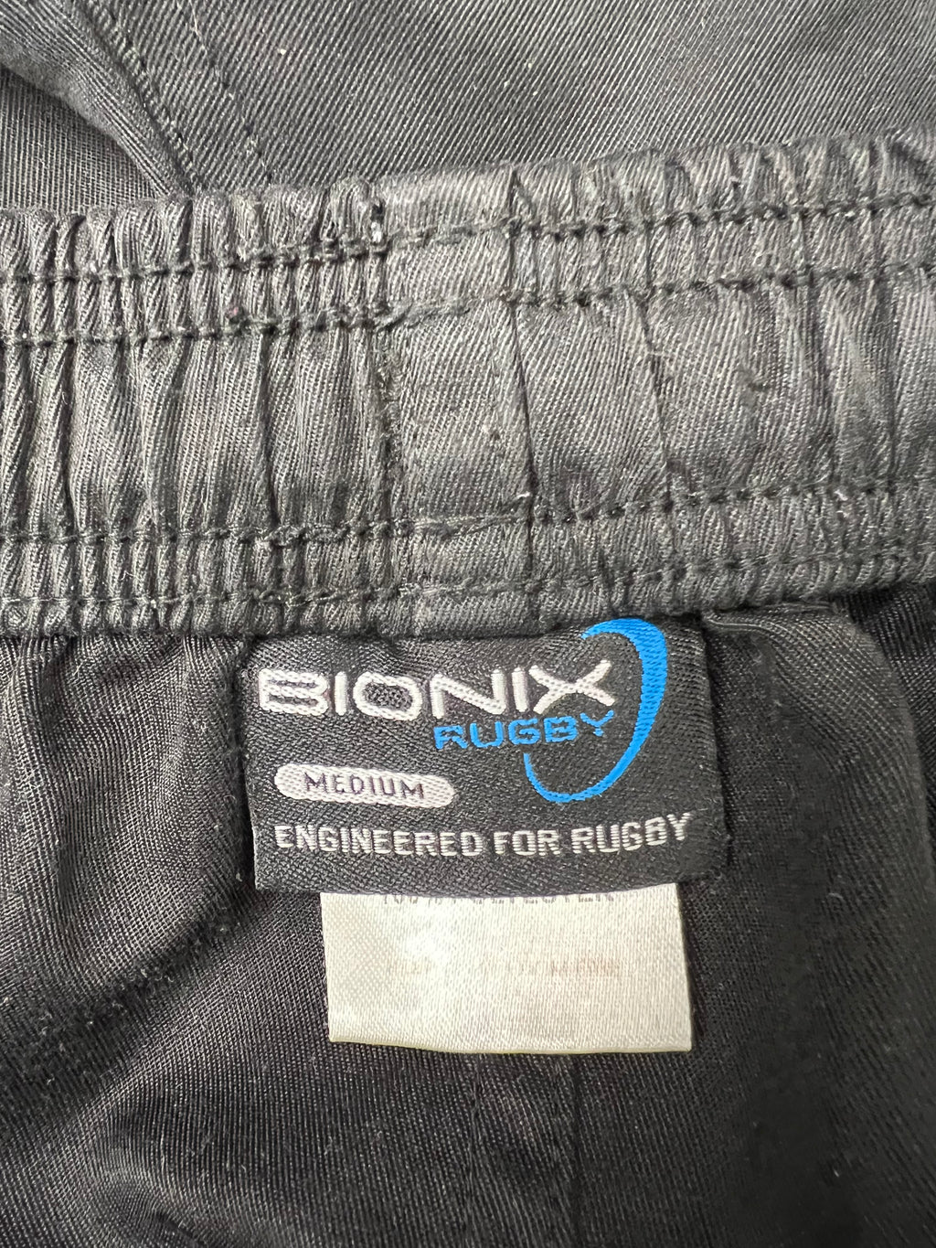 Close-up of Bionix Rugby logo and size label inside black rugby shorts