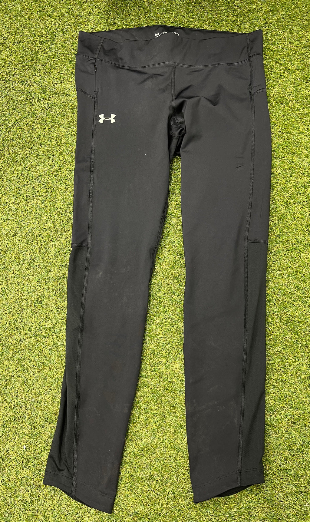 Front view of Under Armour women's black compression leggings laid flat on grass