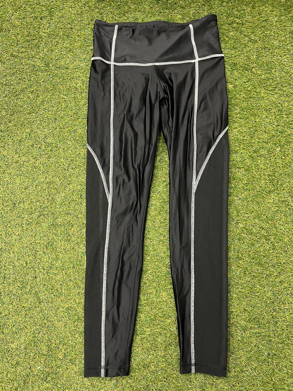 Front view of black Women’s Reebok Speedwick leggings with white stitching laid flat on grass