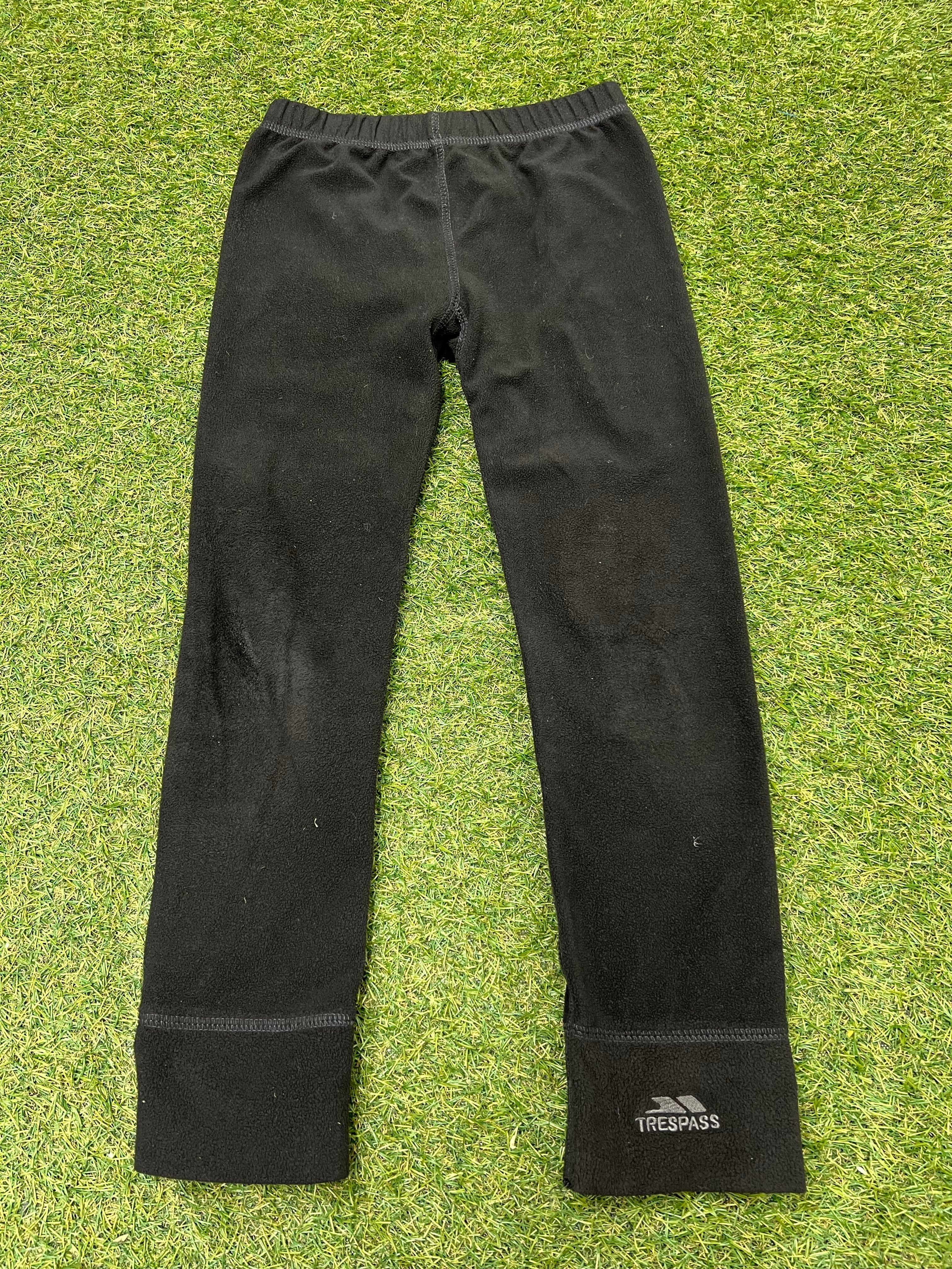 Front view of black kids fleece leggings laid flat on grass showing elastic waistband and straight legs