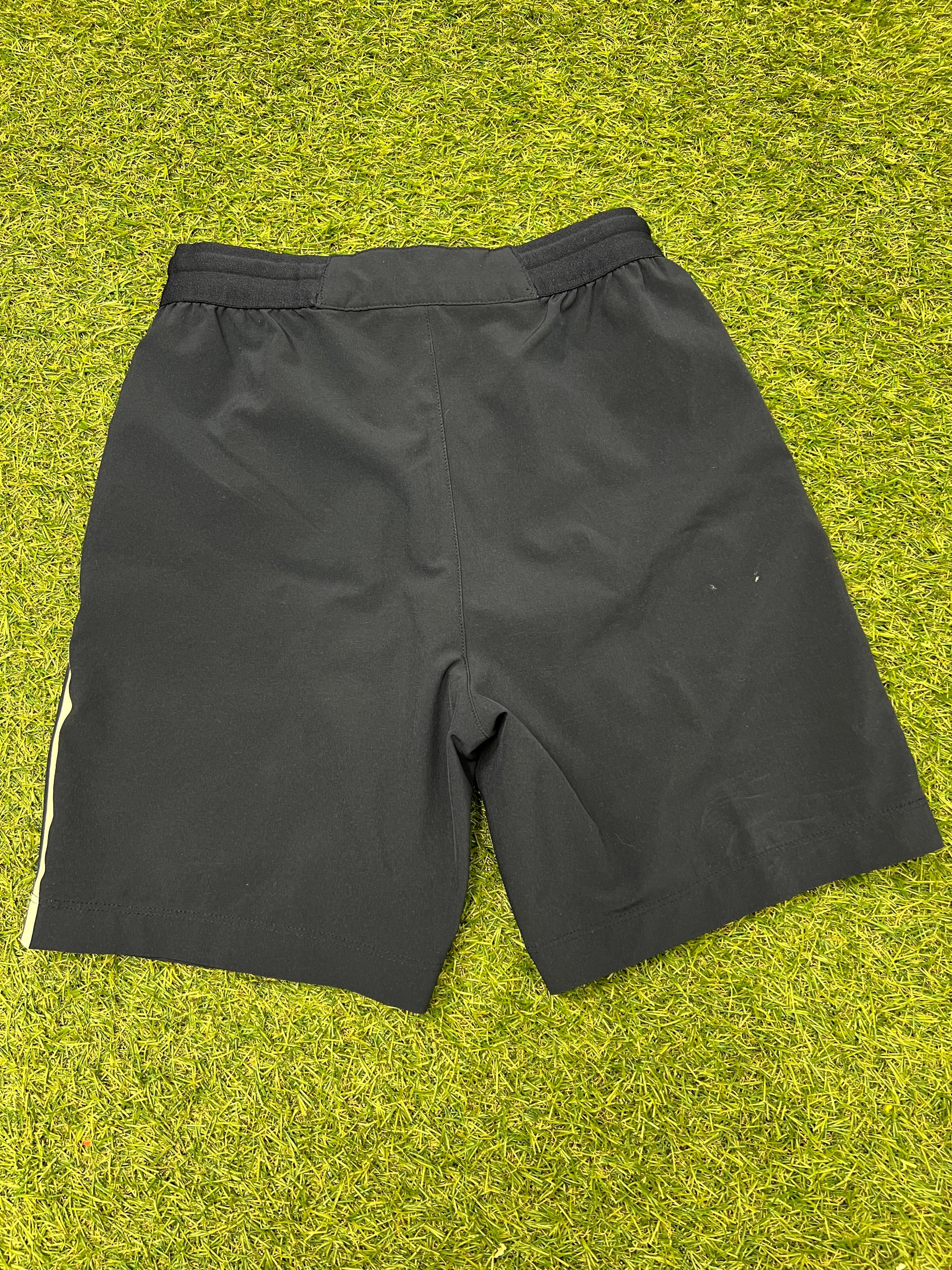 Back view of black Lacoste Roland Garros kids shorts showing elastic waistband on grass