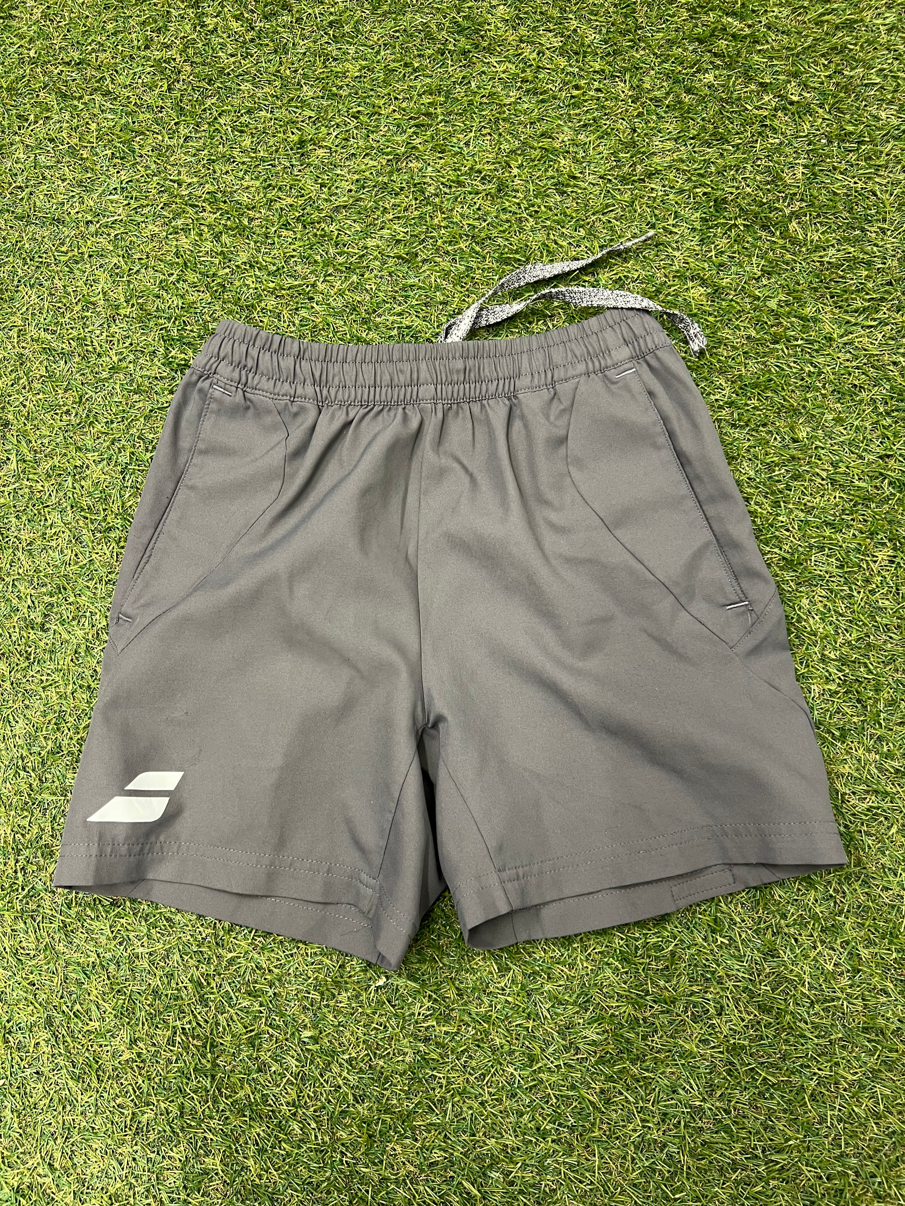Front view of grey Babolat kids training shorts on grass