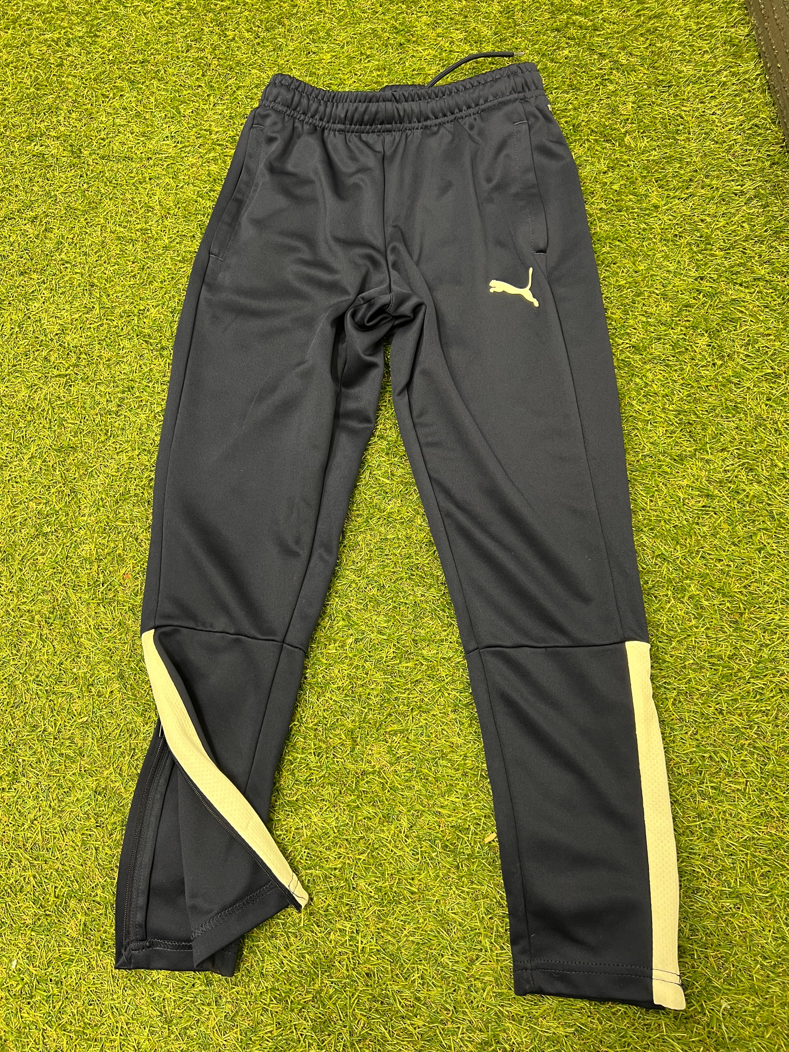 Front view of navy blue kids Puma tracksuit bottoms with light side stripes on green grass