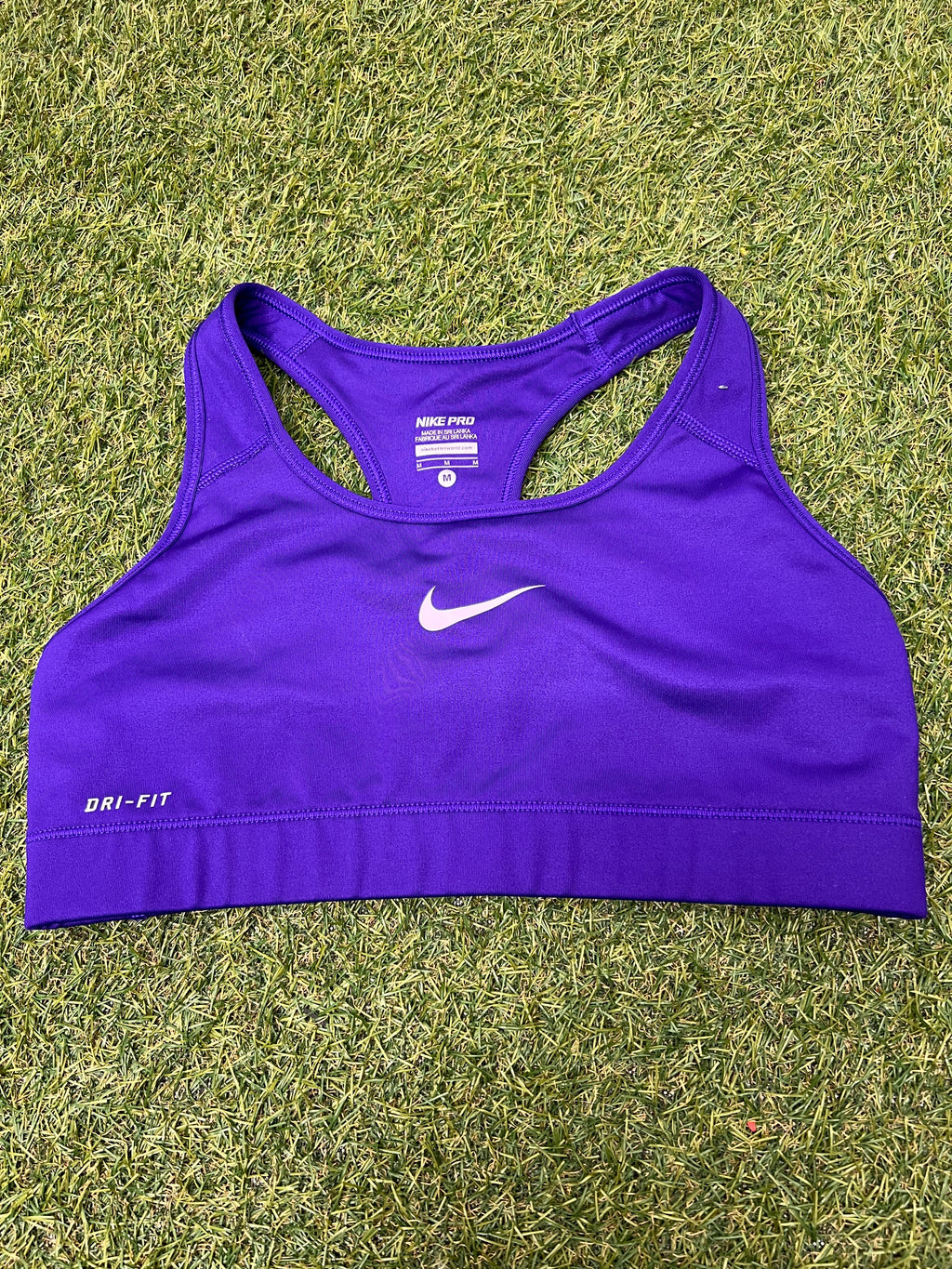 Front view of Nike Pro Dri-FIT purple sports bra laid flat on grass