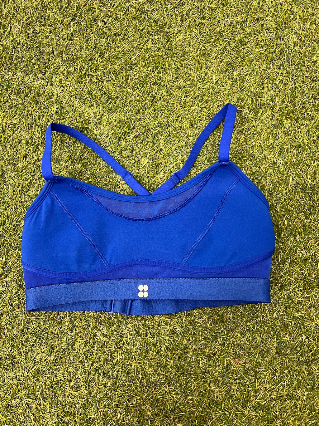 Front view of vibrant blue Sweaty Betty sports bra with thin straps and elastic underband on grass